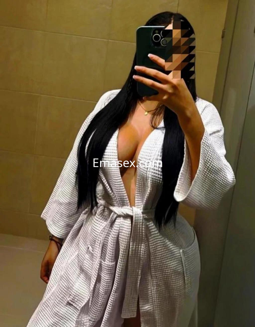 Puta en Sevilla, con cabello largo y oscuro, viste una bata blanca que resalta su escote en un ambiente de baño.
