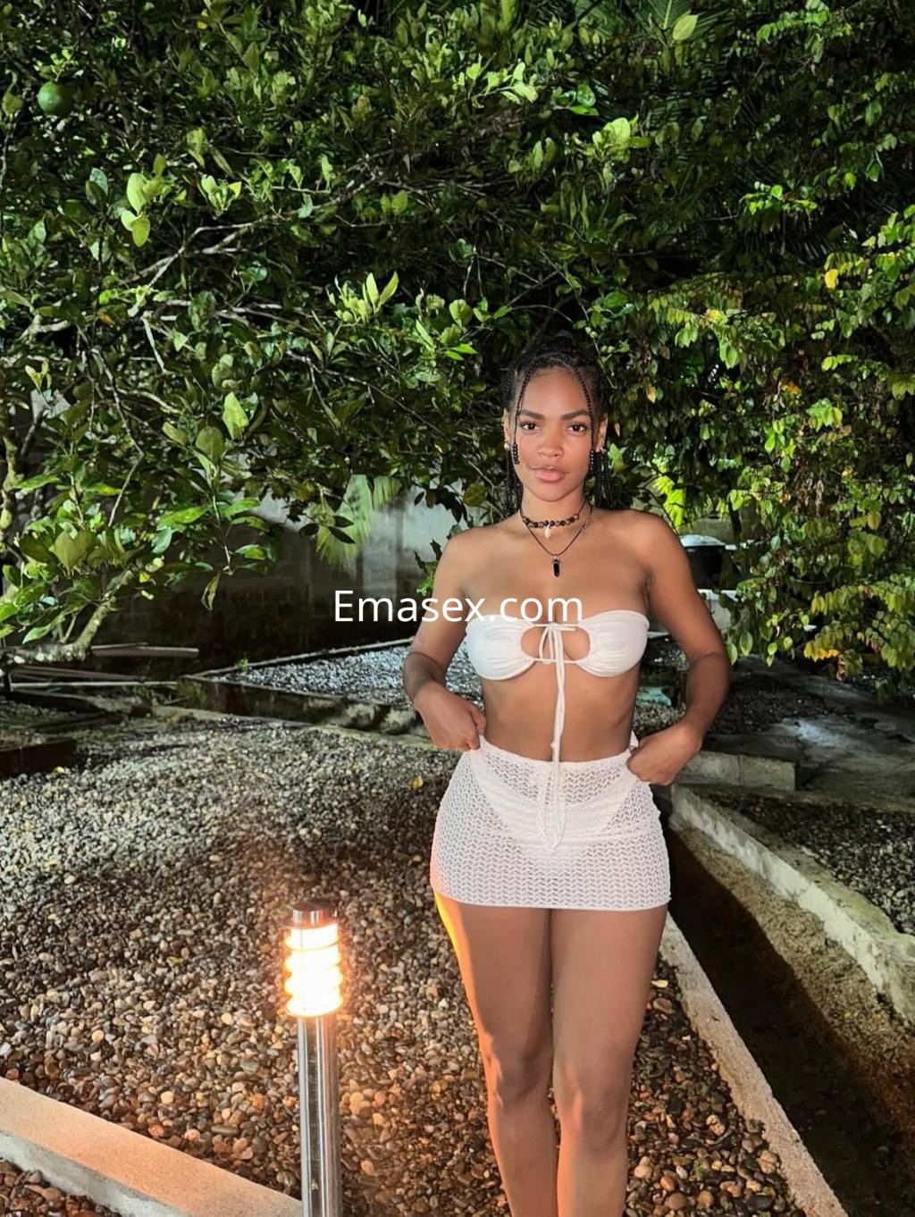 Puta en Tarragona vistiendo un bikini blanco y una falda de crochet, posando con confianza en un entorno natural.