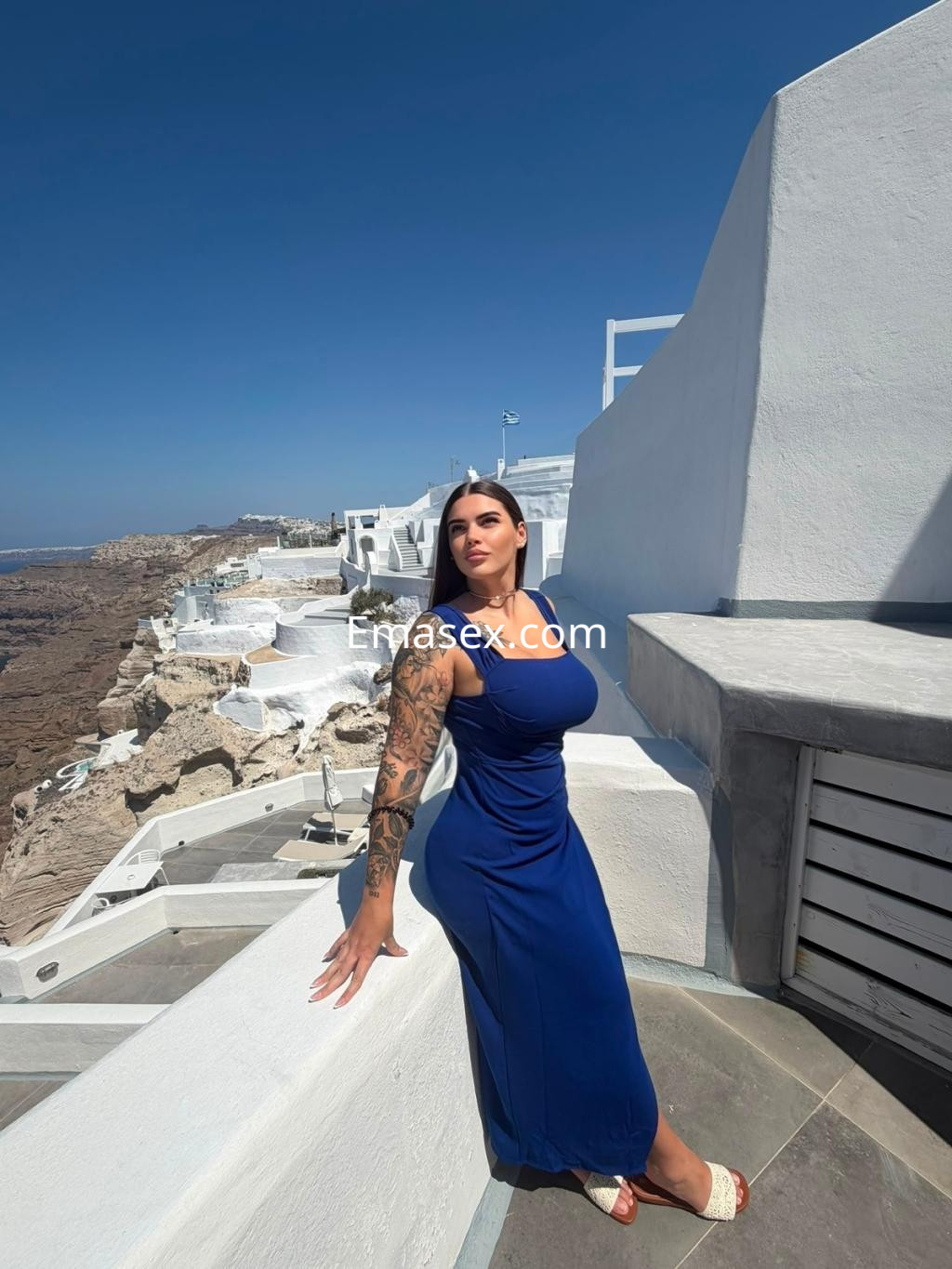Escort en Vigo, con cabello largo y suelto, vistiendo un vestido azul, posando en un paisaje costero.