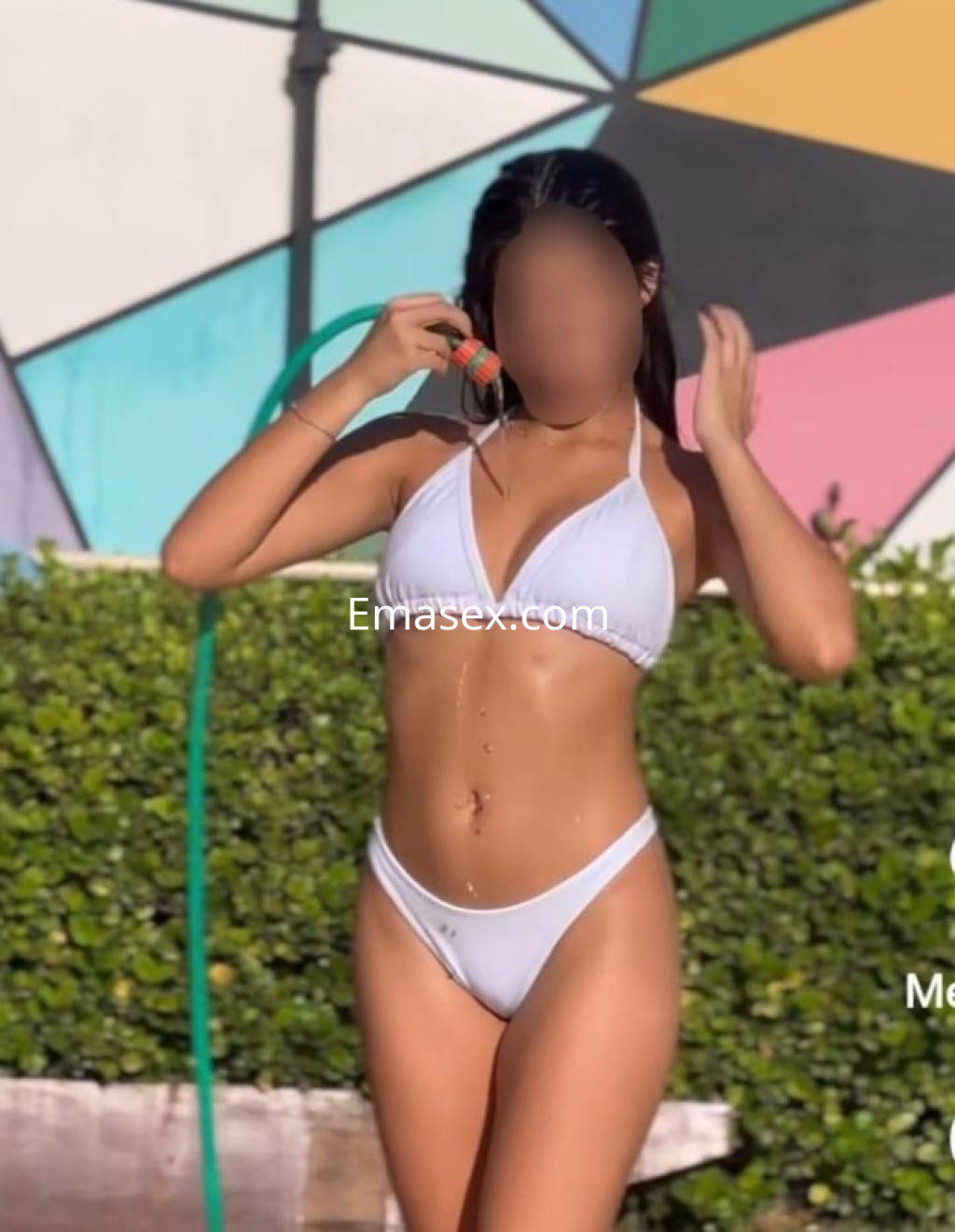 Escort en Tarragona con bikini blanco, posando junto a una manguera y un fondo colorido.