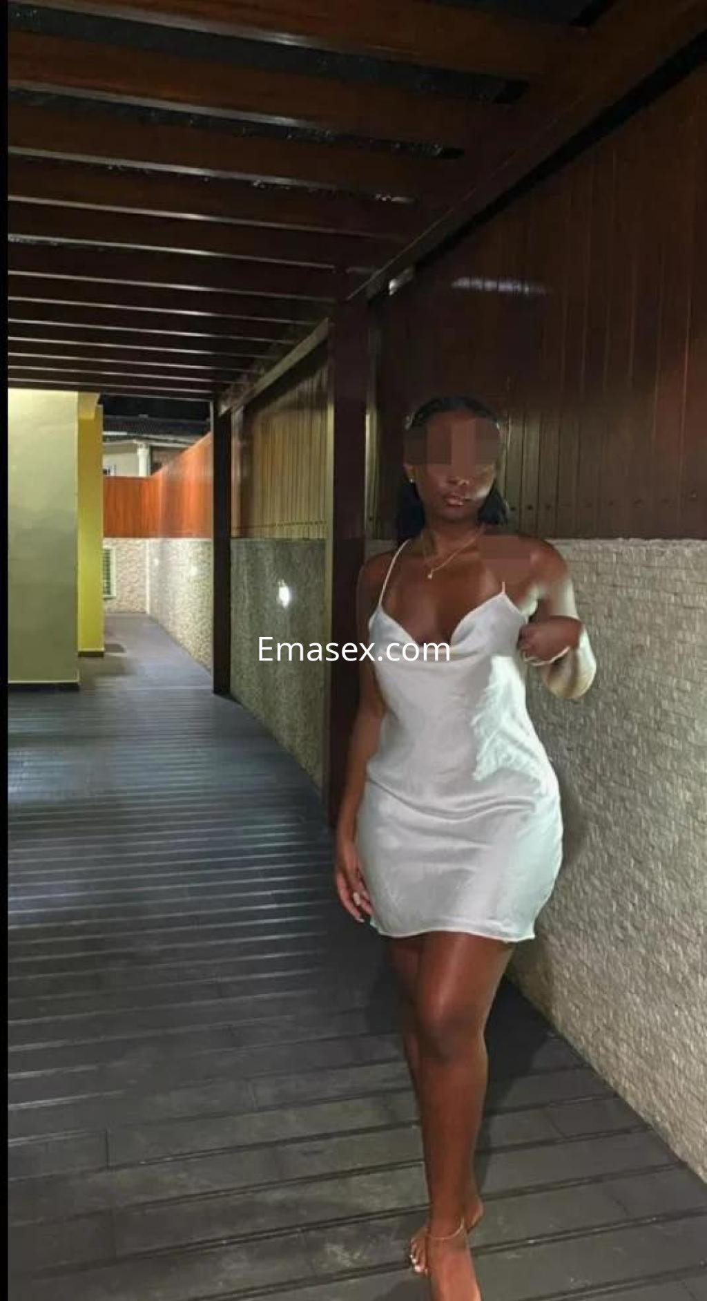 Puta en Madrid camina por un pasillo con paredes de madera, luciendo un vestido blanco ajustado.