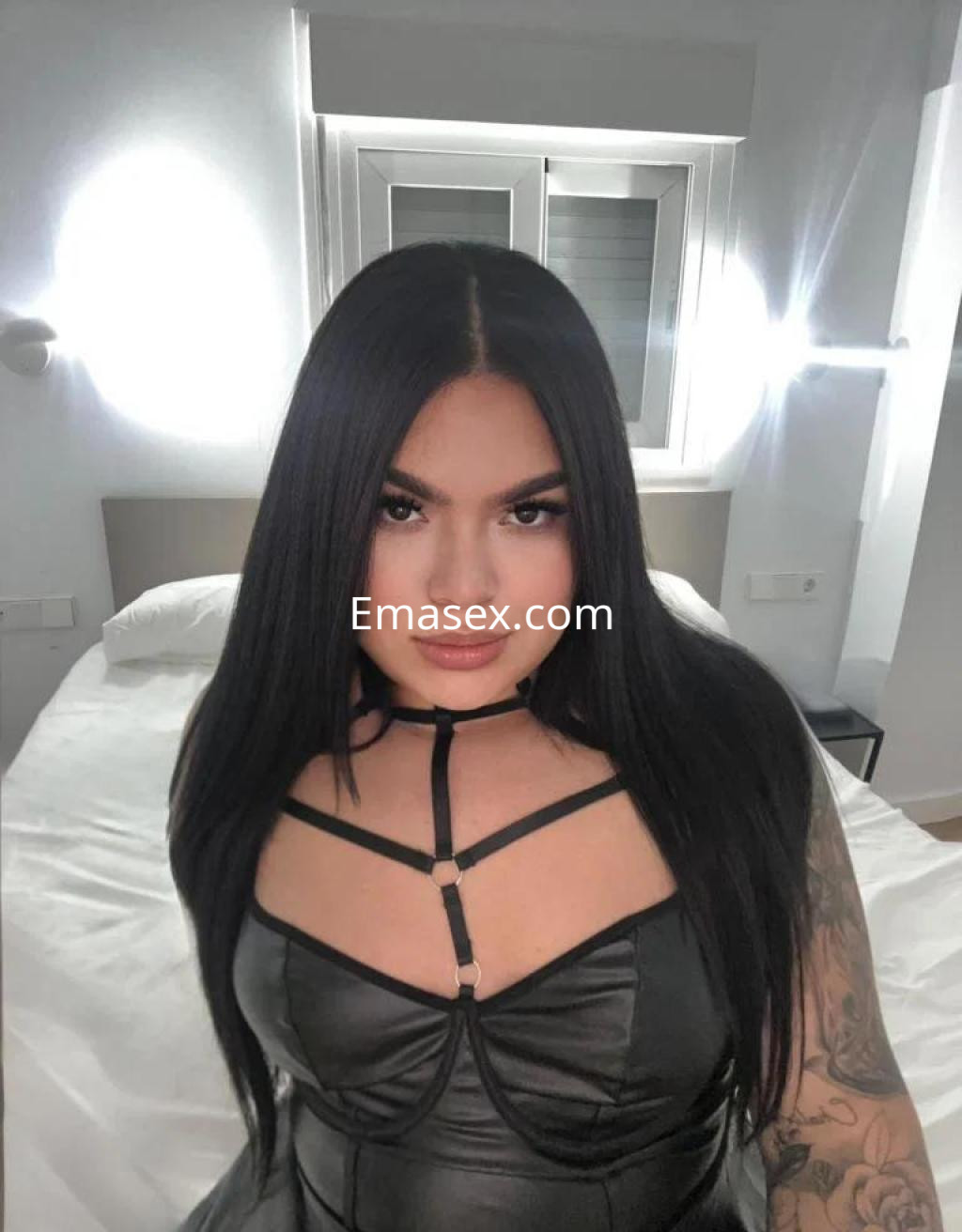La puta en Murcia lleva un vestido negro ajustado con tiras, posando en una habitación iluminada.