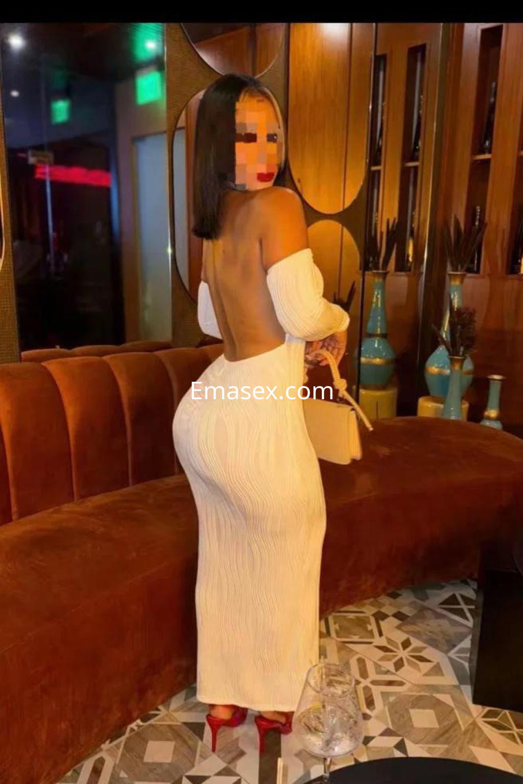 Escort en Almería con vestido blanco de manga larga y escote en la espalda, posando en un salón elegante.