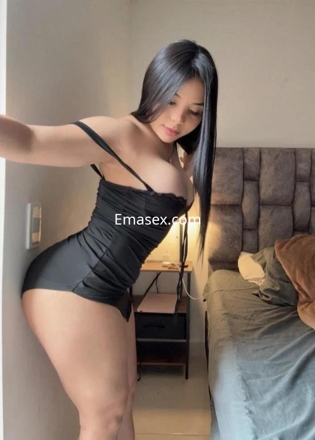 Escort en Alicante con cabello largo y lacio, vistiendo un vestido negro ajustado en un ambiente acogedor.