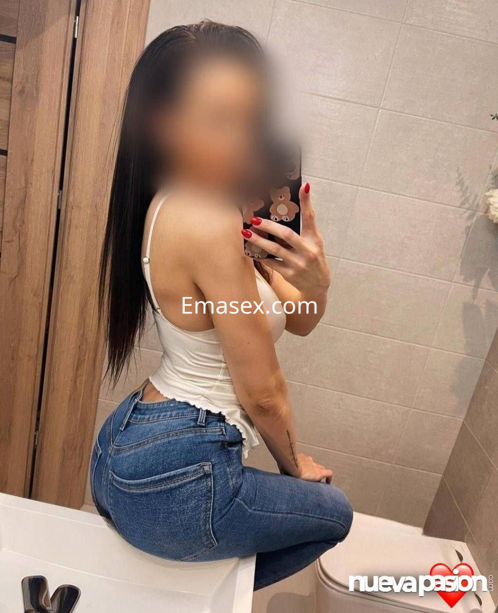 La puta posa en un baño, vistiendo una camiseta blanca y jeans ajustados, con el cabello largo y lacio en Sevilla.