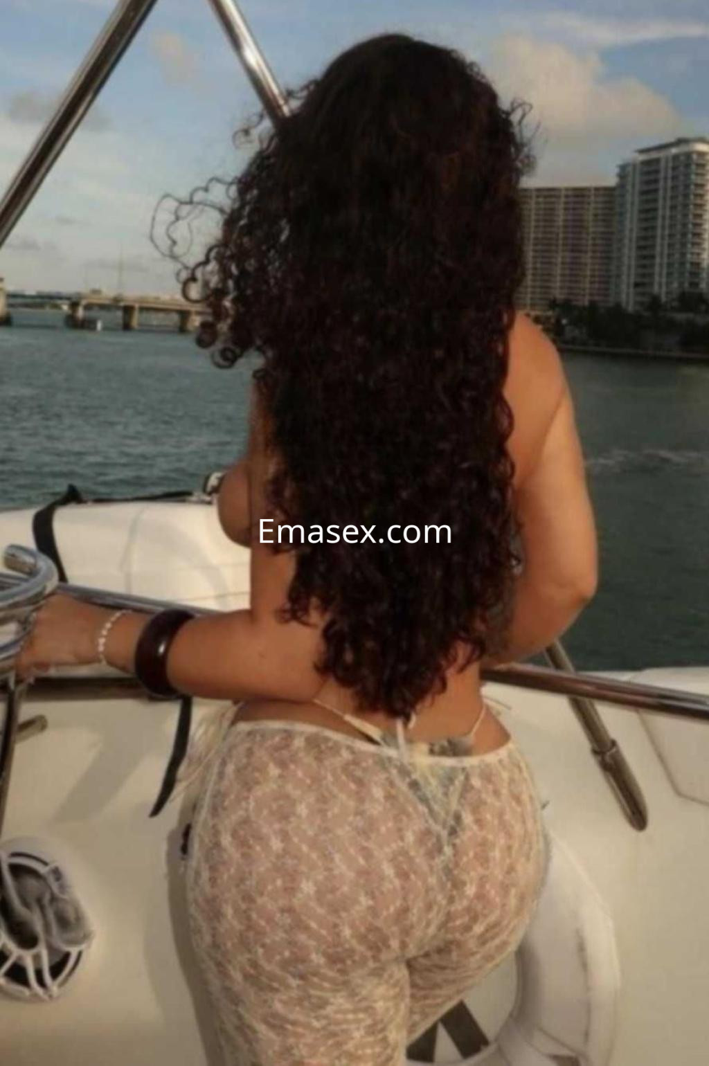 Puta con cabello rizado y oscuro, de espaldas en un barco, vistiendo una prenda transparente, en Madrid.