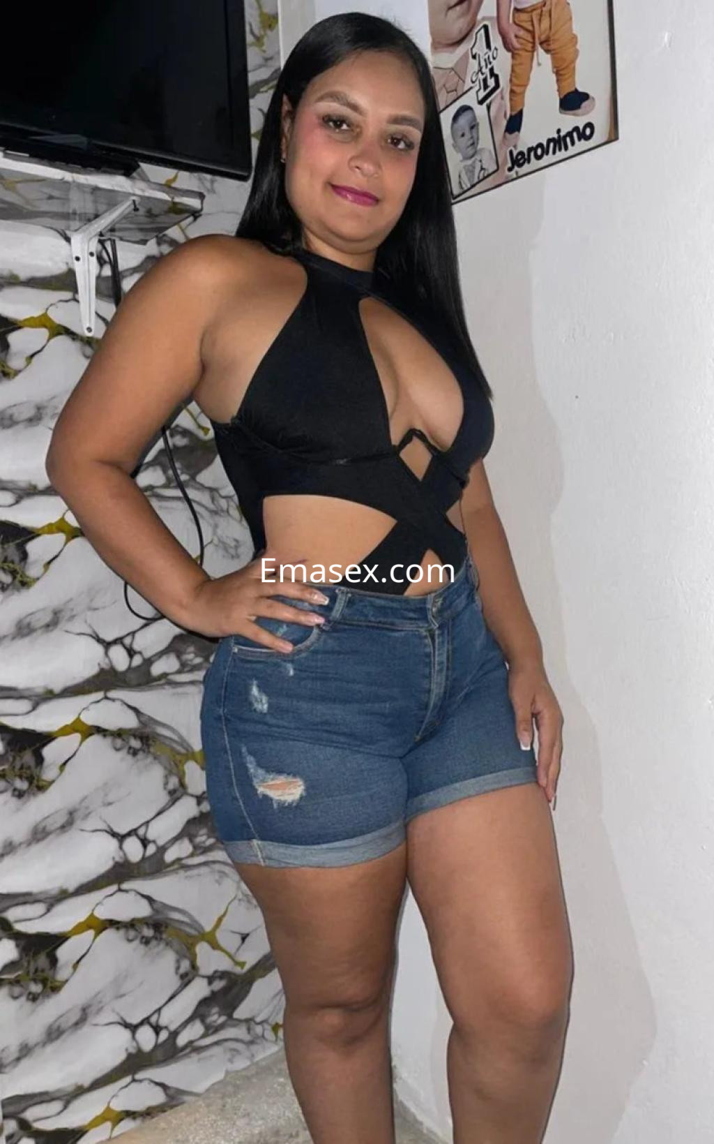 Puta con cabello lacio y negro, viste un top negro con cortes y shorts de mezclilla, posando en Cádiz.