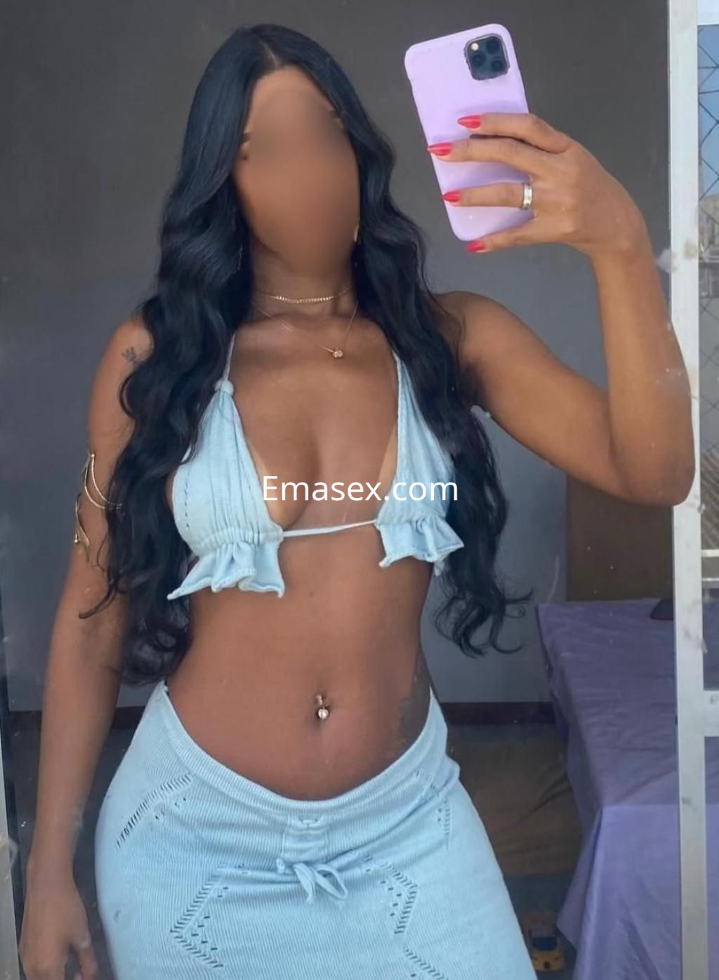 Escort en Cádiz con cabello largo y ondulado, luciendo un conjunto de dos piezas en color celeste mientras se toma una selfie.