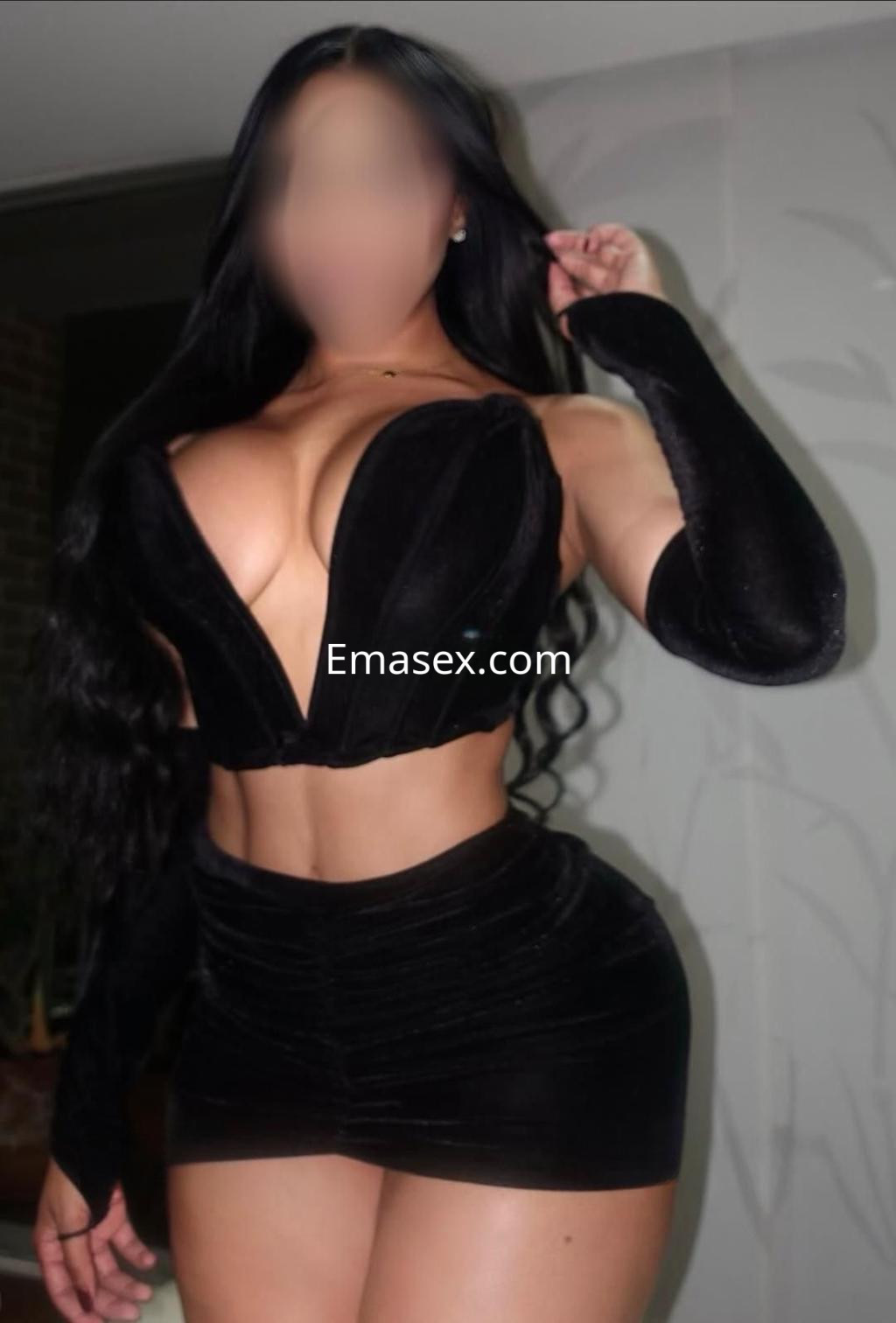 Puta con cabello largo y ondulado, viste un conjunto negro ajustado que resalta su figura en Granada.