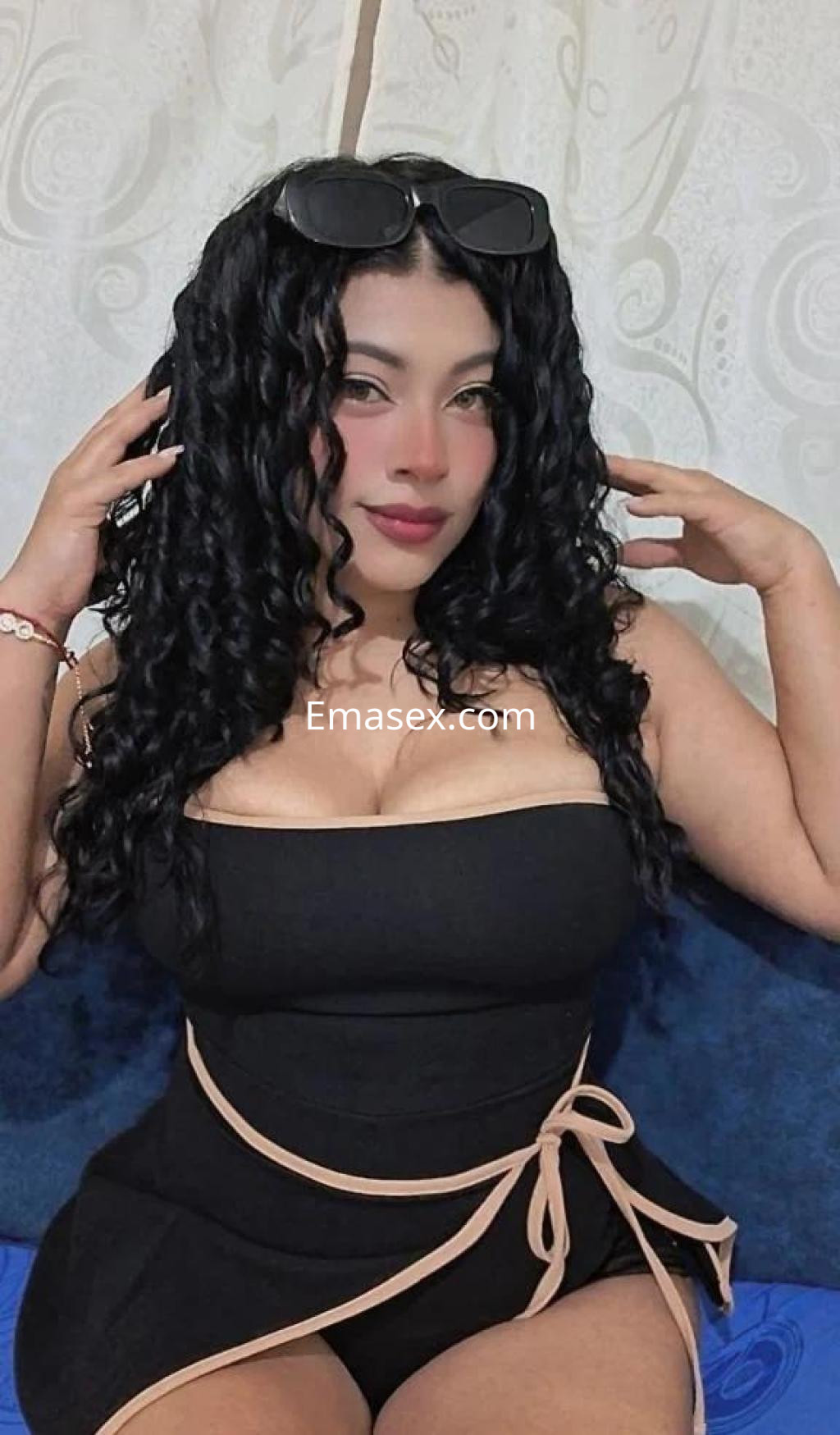 Escort en Barcelona con cabello rizado y oscuro, viste un ajustado mono negro con detalles en la cintura.