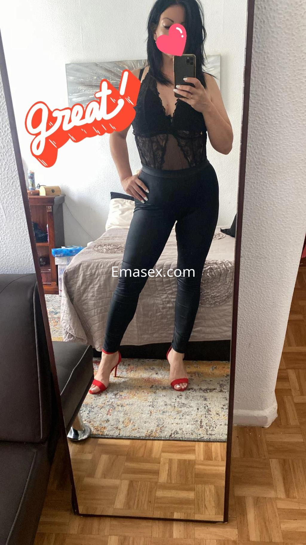 La puta en Donosti luce un body de encaje negro y leggings ajustados, posando en un espejo con tacones rojos.