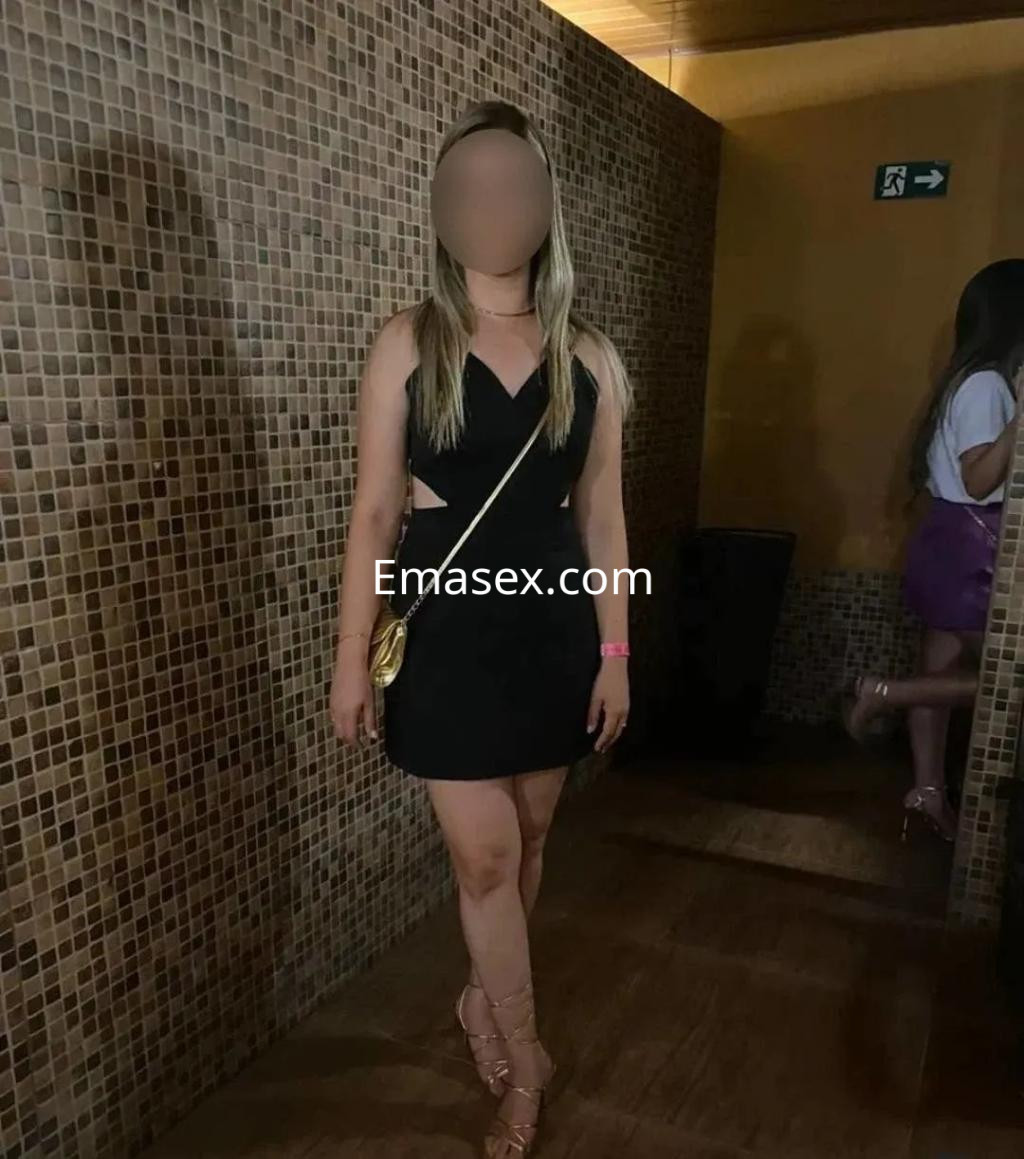 Escort en Albacete, luciendo un vestido negro ajustado con detalles en los costados y sandalias de tiras.