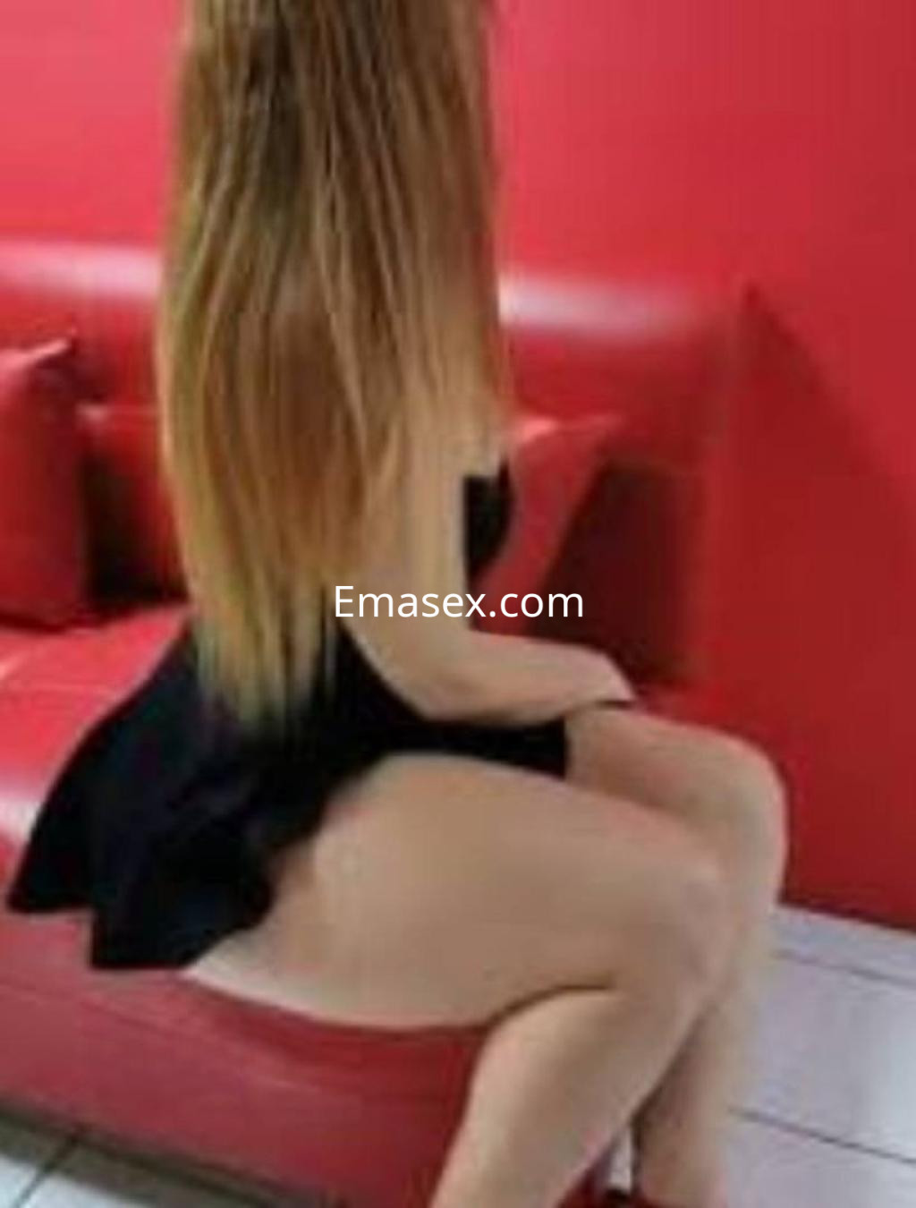 Puta con cabello largo y lacio, vestida con un vestido negro, sentada en un sofá rojo en Barcelona.