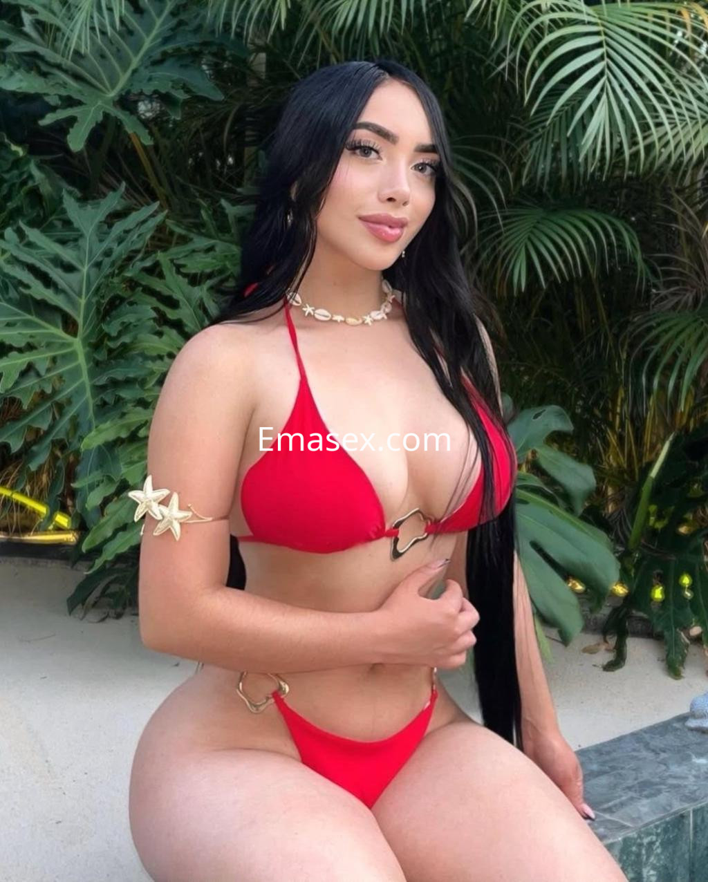 Escort en Logroño, posando con un bikini rojo, cabello largo y lacio, rodeada de plantas tropicales.