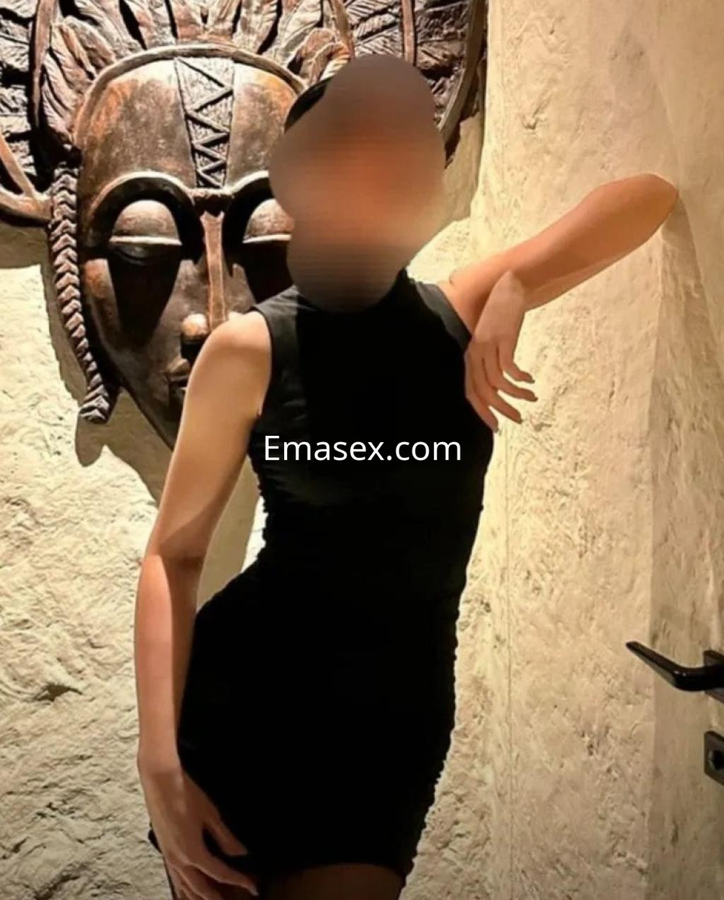 La escort viste un vestido negro ajustado mientras posa con una mano en la cadera frente a una decoración artística en Zaragoza.