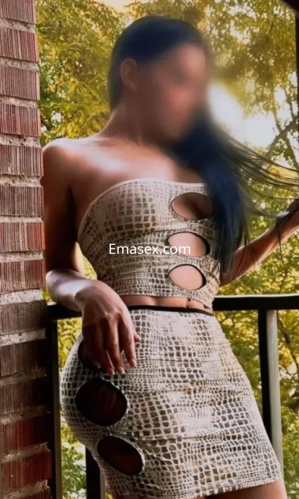 Puta en Madrid luciendo un vestido ajustado de estampado de serpiente con cortes laterales, posando en un balcón.