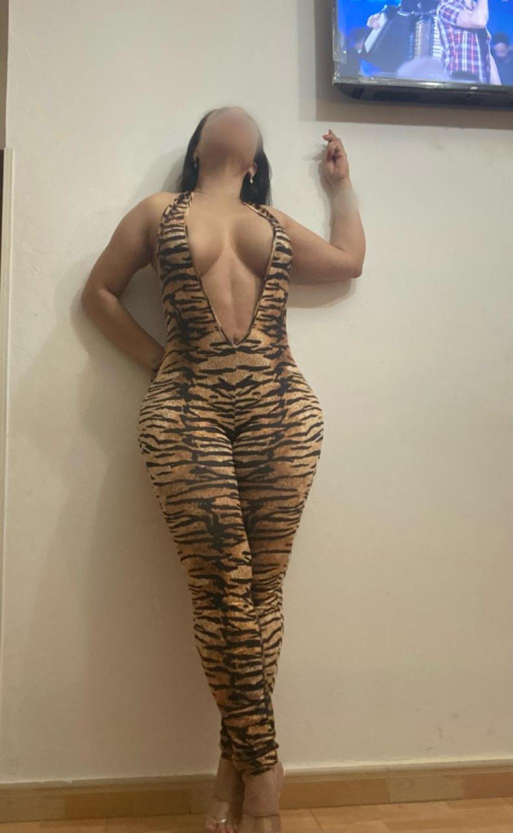 Puta de Santander luciendo un catsuit ajustado de estampado de tigre, con tacones y pose atrevida.