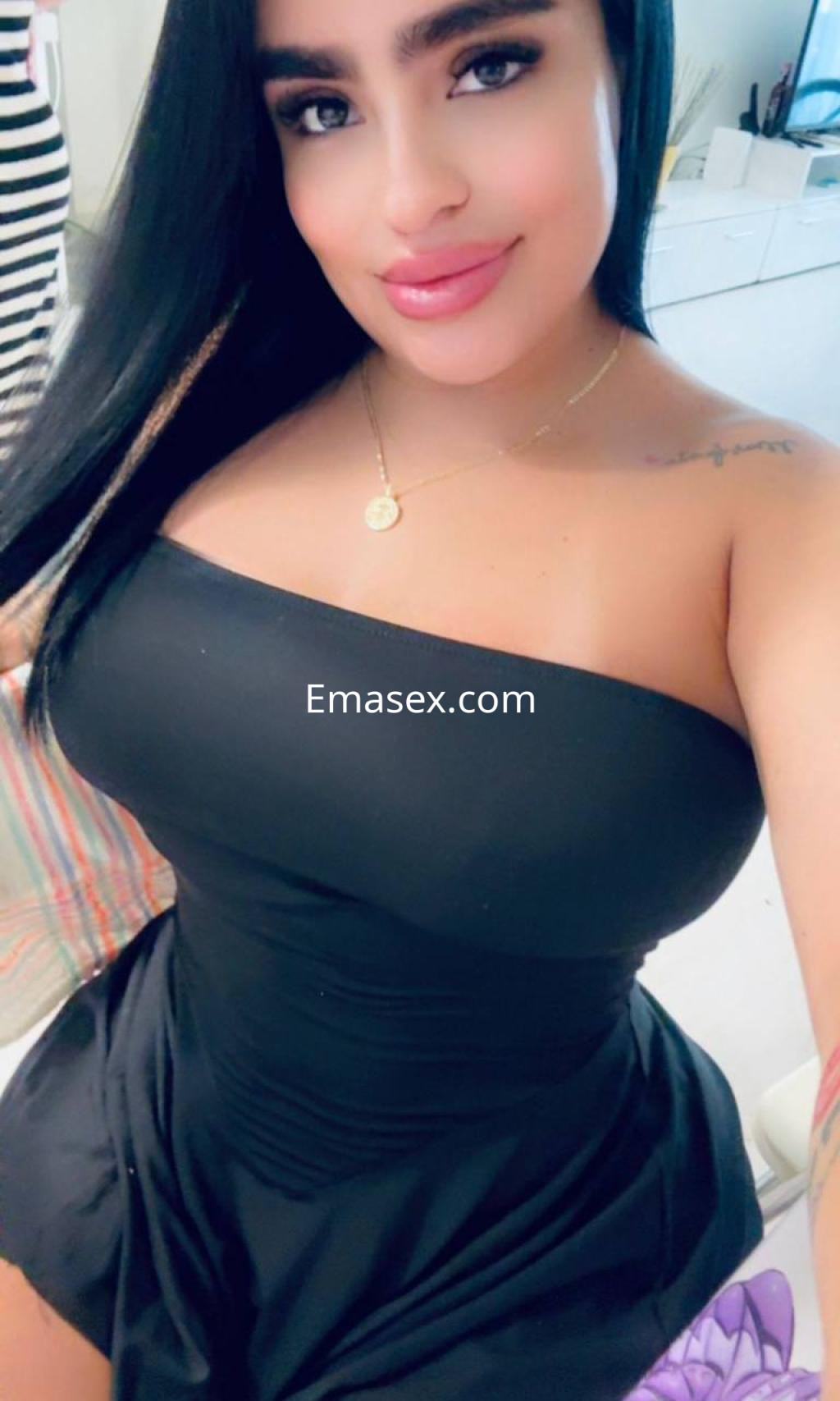 Puta en Donosti con vestido negro ajustado, cabello largo y lacio, sonriendo en un ambiente interior.