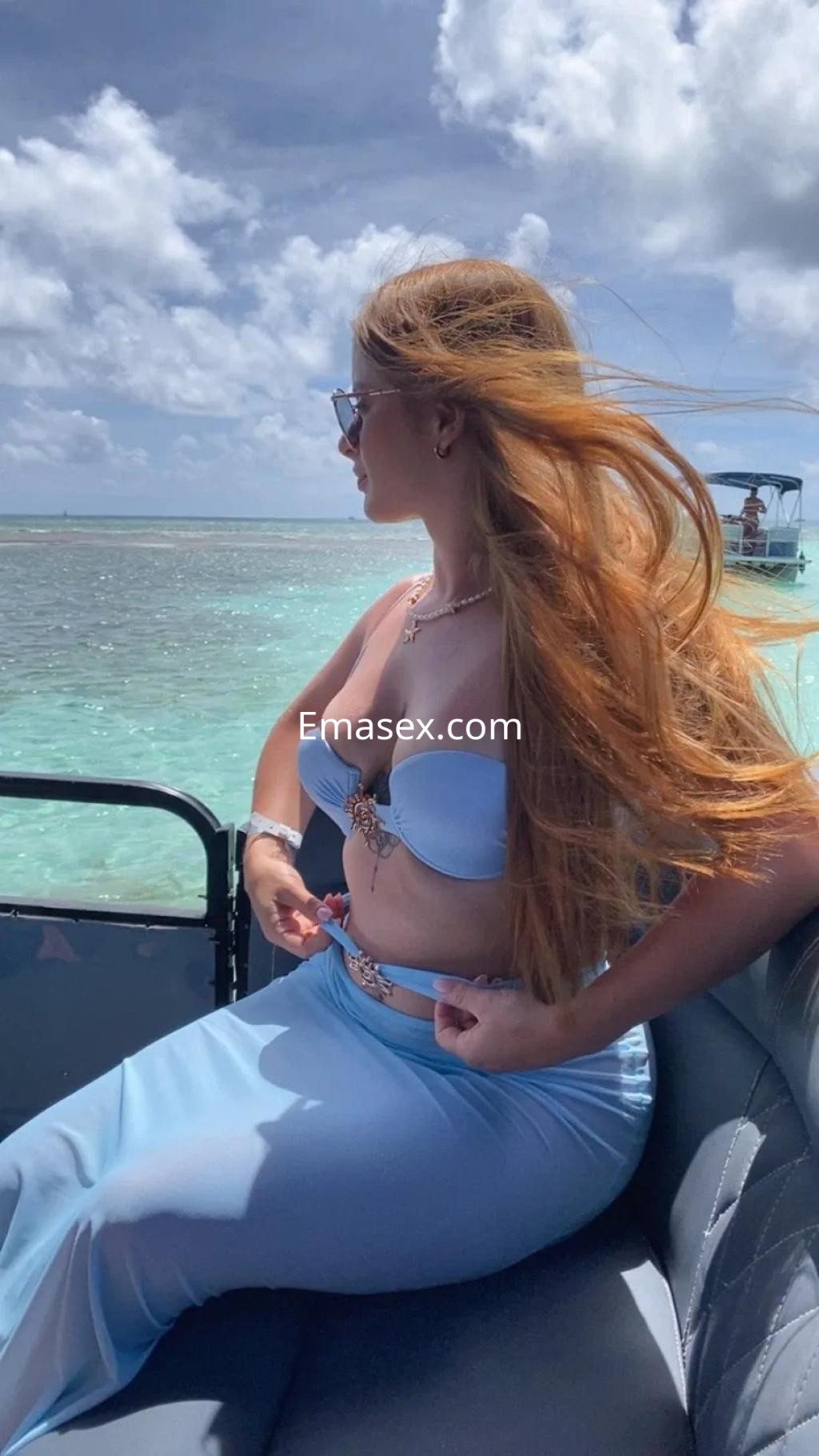 Escort con cabello largo y suelto, vistiendo un bikini azul, disfruta del sol en un barco en Sevilla.