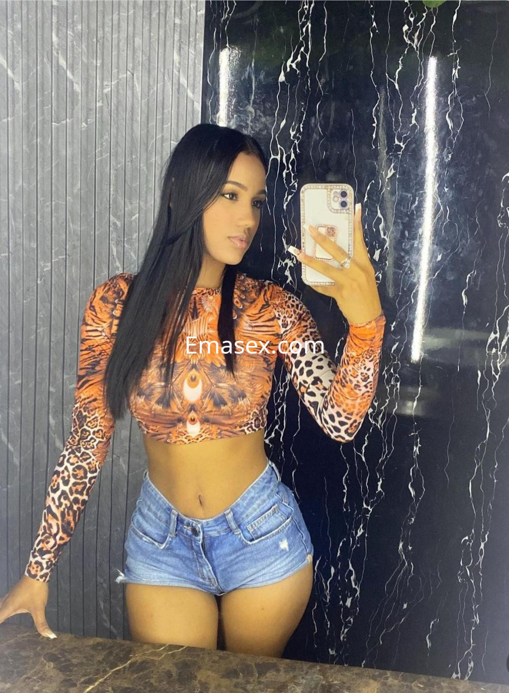 Puta con cabello largo y lacio, viste un top de estampado animal y shorts de mezclilla, en un baño de Santander.