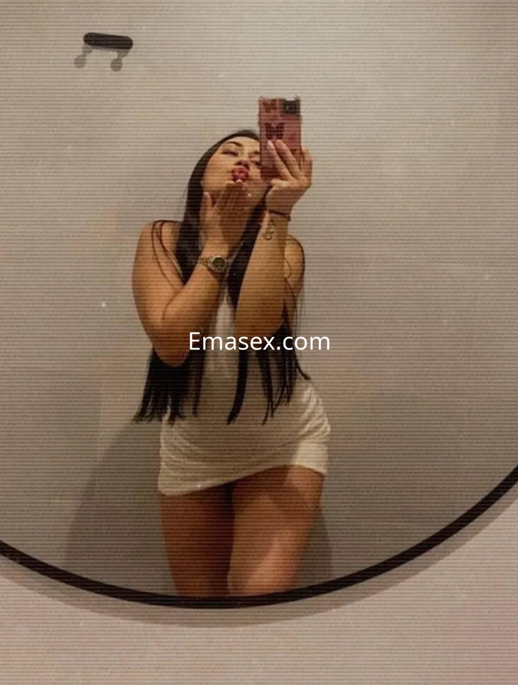 La puta posa frente a un espejo con un vestido blanco, mostrando su cabello largo y una actitud coqueta en Palma de Mallorca.