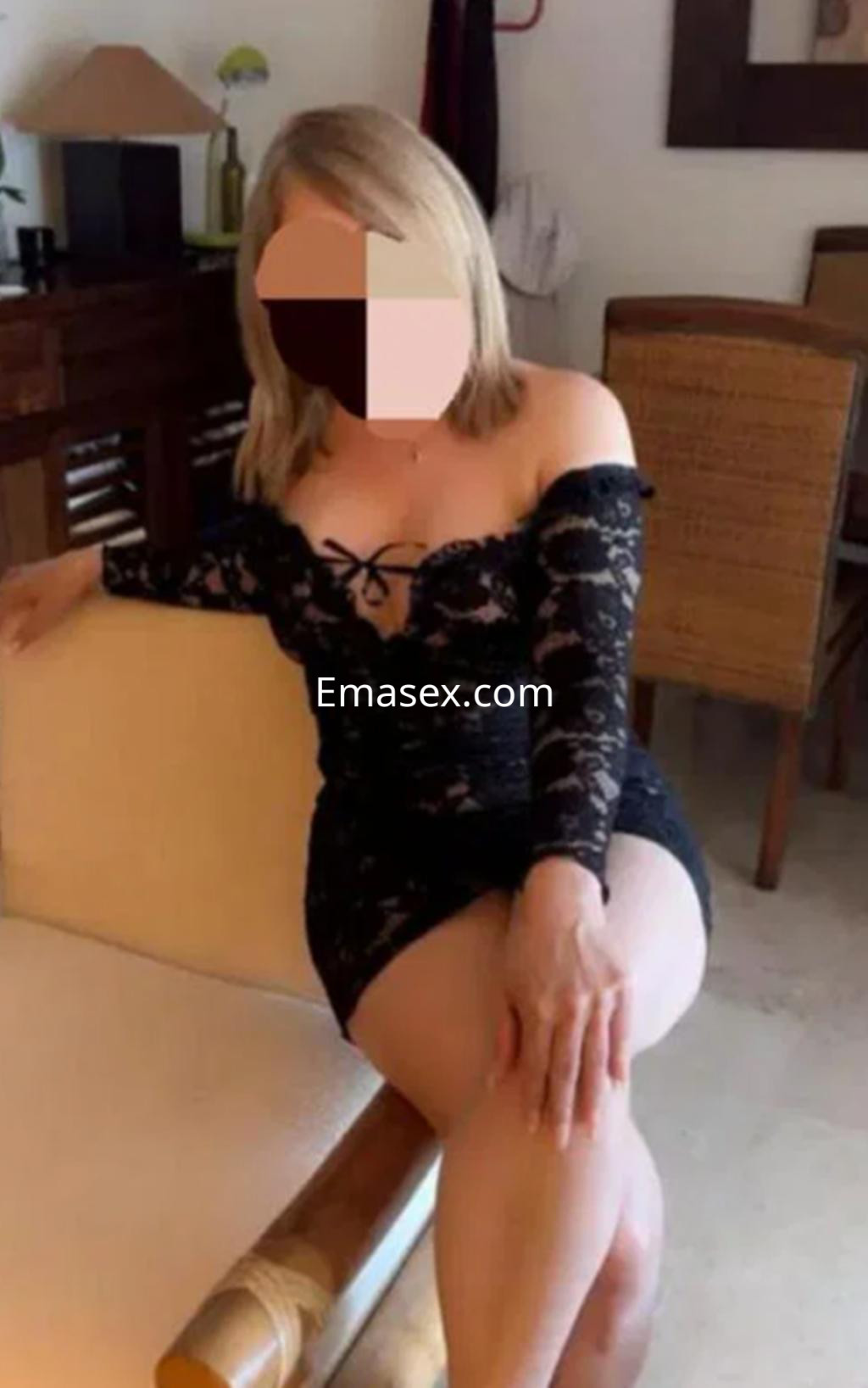 Escort en Logroño sentada en una silla con un vestido de encaje negro, mostrando una postura elegante y coqueta.