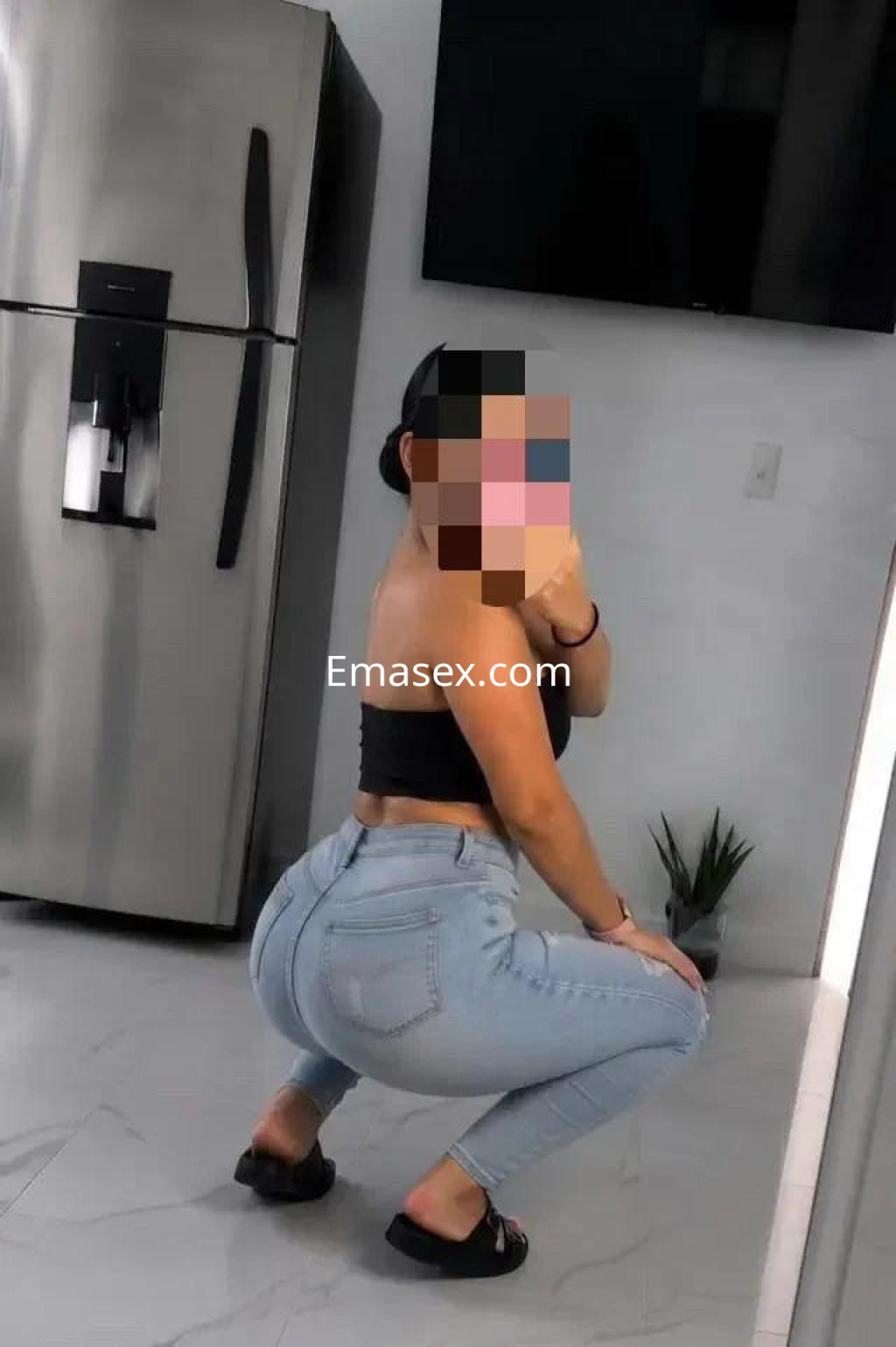 Escort en Albacete posando de perfil con top negro y jeans ajustados en un ambiente moderno y luminoso.
