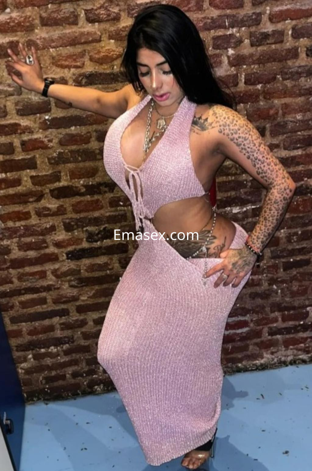 Escort en Castellón con un vestido largo de color rosa, mostrando tatuajes en su piel y una pose sugestiva.
