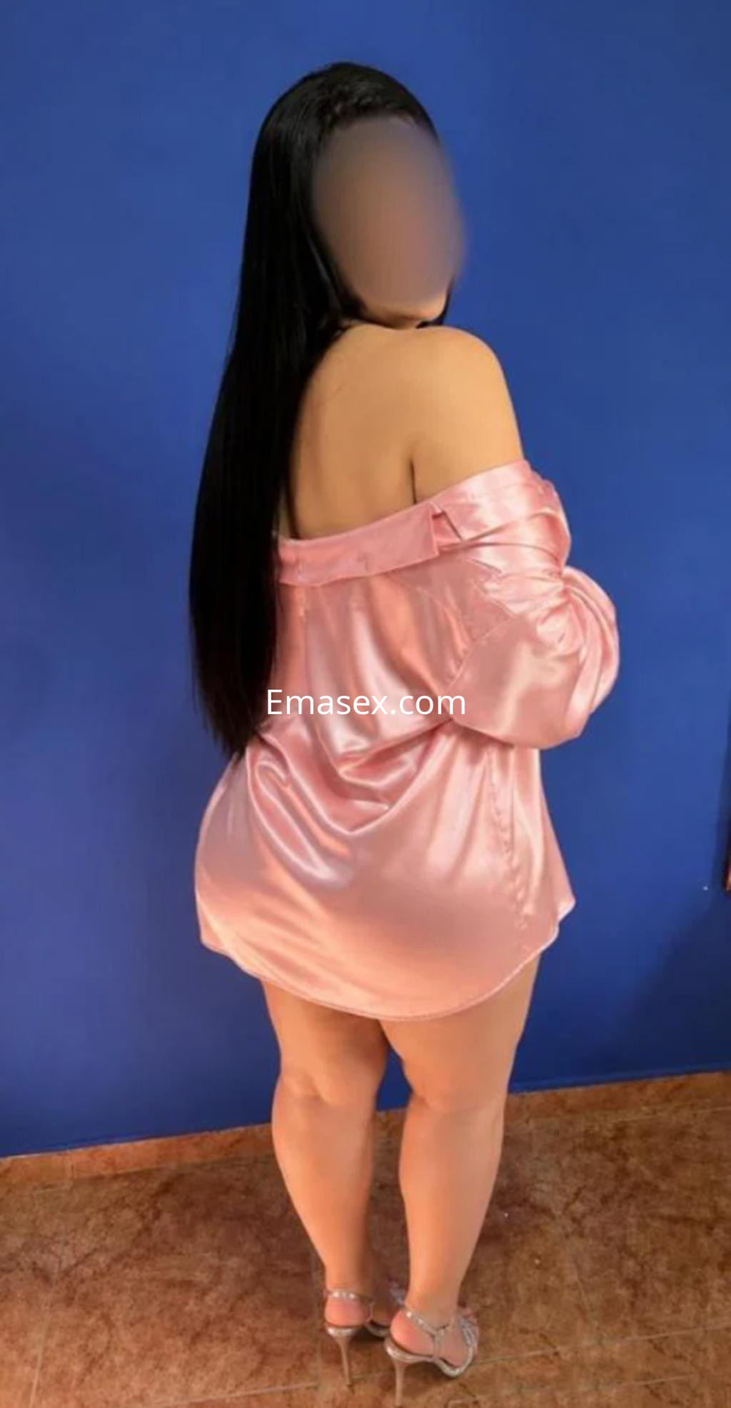 Escort en Pamplona con cabello largo y lacio, vistiendo una camisa de seda rosa y tacones, de espaldas a la cámara.