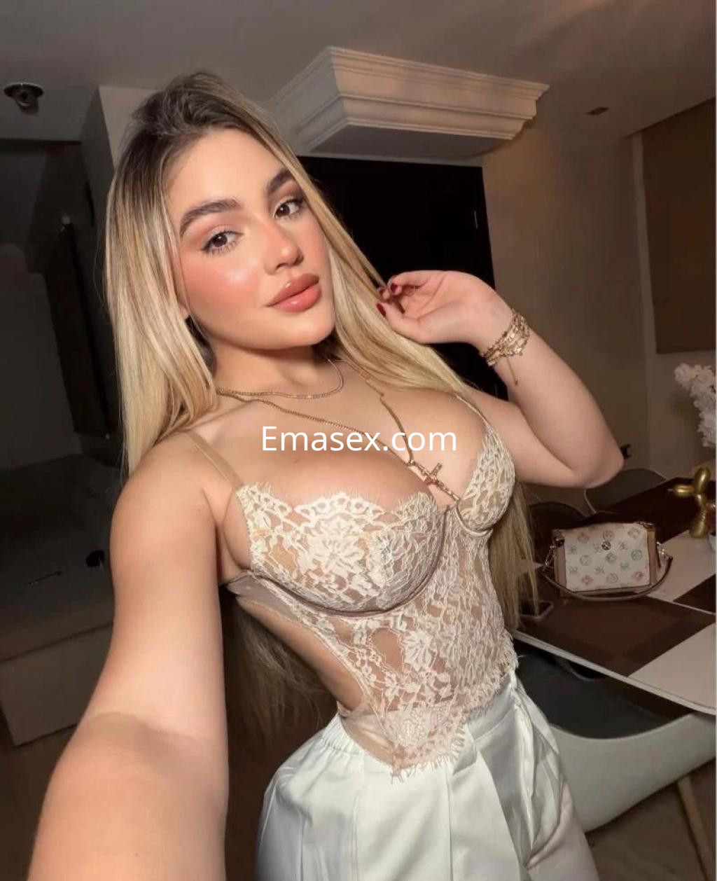 Puta con cabello largo y rubio, vestida con un body transparente, posando en un ambiente moderno en Málaga.