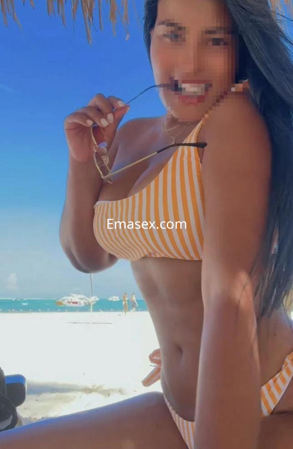 Escort en Málaga con bikini de rayas amarillas y blancas, posando en la playa con el mar de fondo.