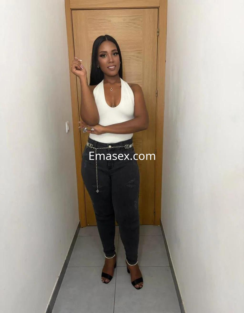 Escort en Málaga luciendo una blusa blanca y jeans oscuros, posando con confianza en un pasillo.