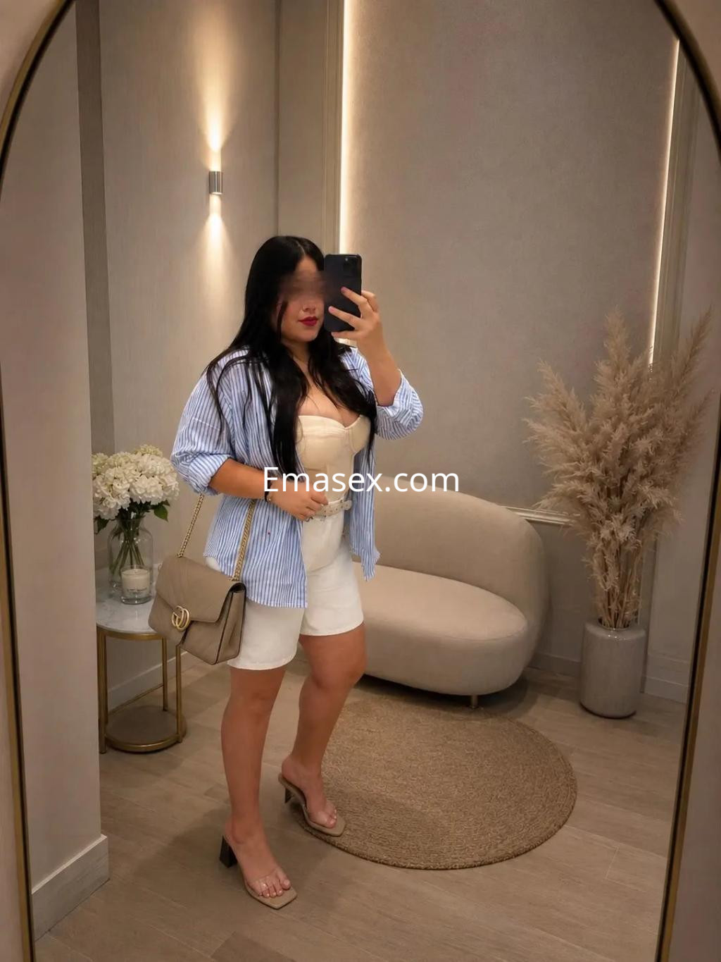 Puta en Valladolid luciendo un conjunto claro con una blusa de rayas y shorts cortos en un entorno moderno.