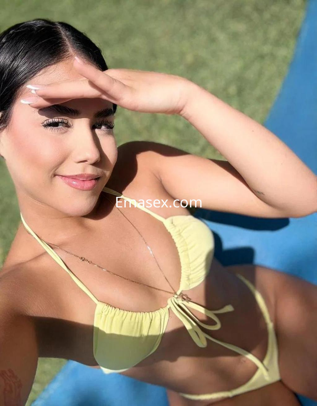 Puta en Tarragona con un bikini amarillo, posando al sol y sonriendo mientras se protege del resplandor.