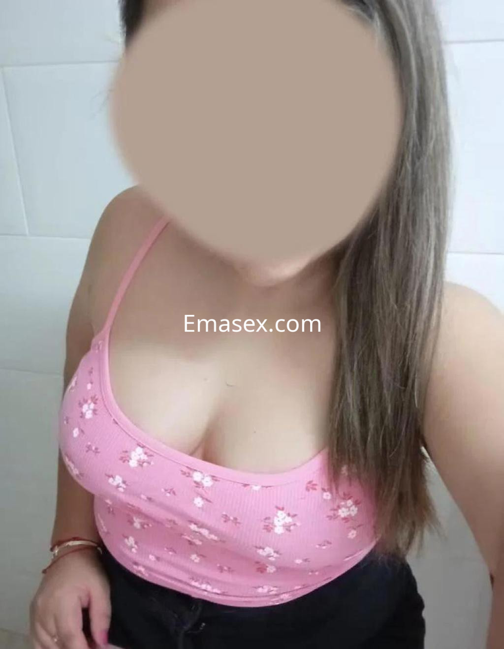Escort en León con cabello lacio y castaño, viste un top rosa con flores y pantalones oscuros.