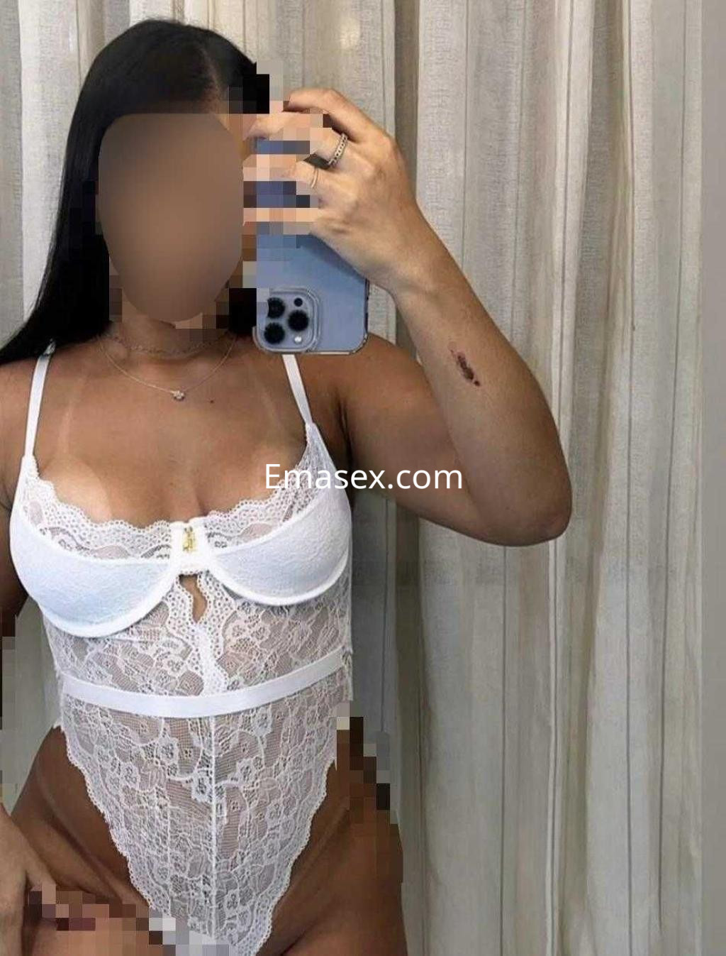 La puta en Sevilla luce un conjunto de lencería blanca con encaje, posando frente a un espejo.