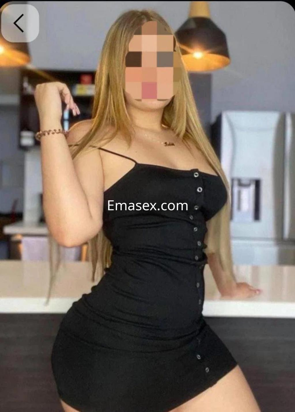 Puta de cabello largo y lacio, viste un vestido negro ajustado con botones, posando en una cocina moderna en Cáceres.