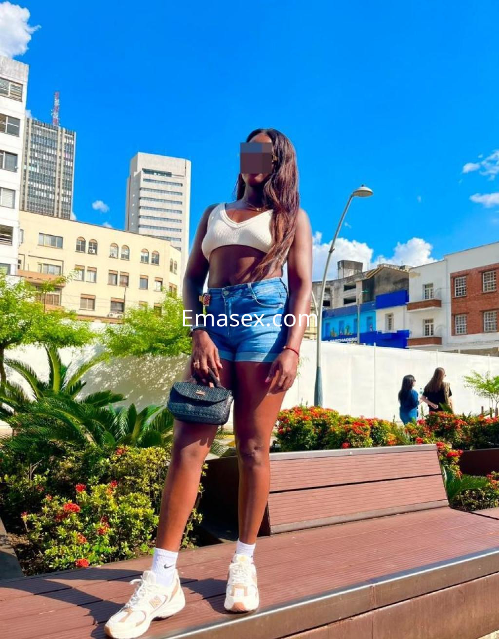 Puta en Cáceres con top blanco y shorts de mezclilla, posando al aire libre con un fondo urbano.