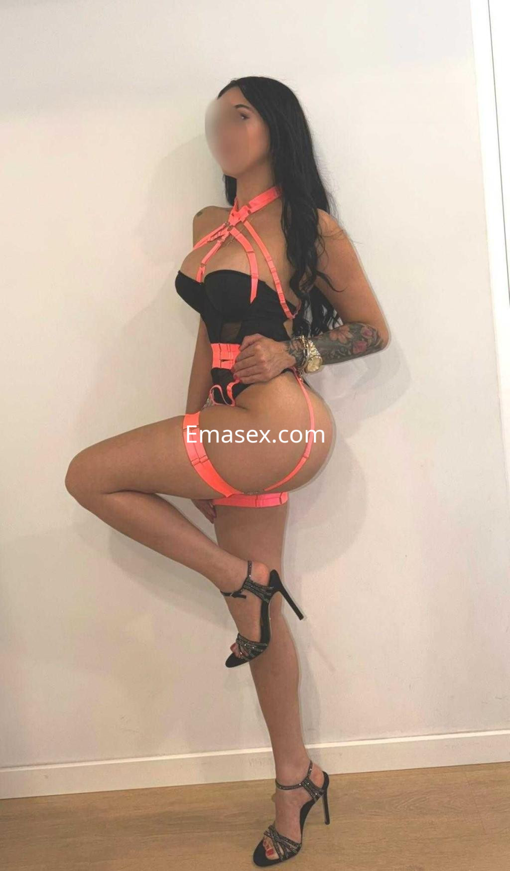 La puta luce un conjunto de lencería negra con detalles en rosa y tacones altos en un entorno minimalista en Barcelona.