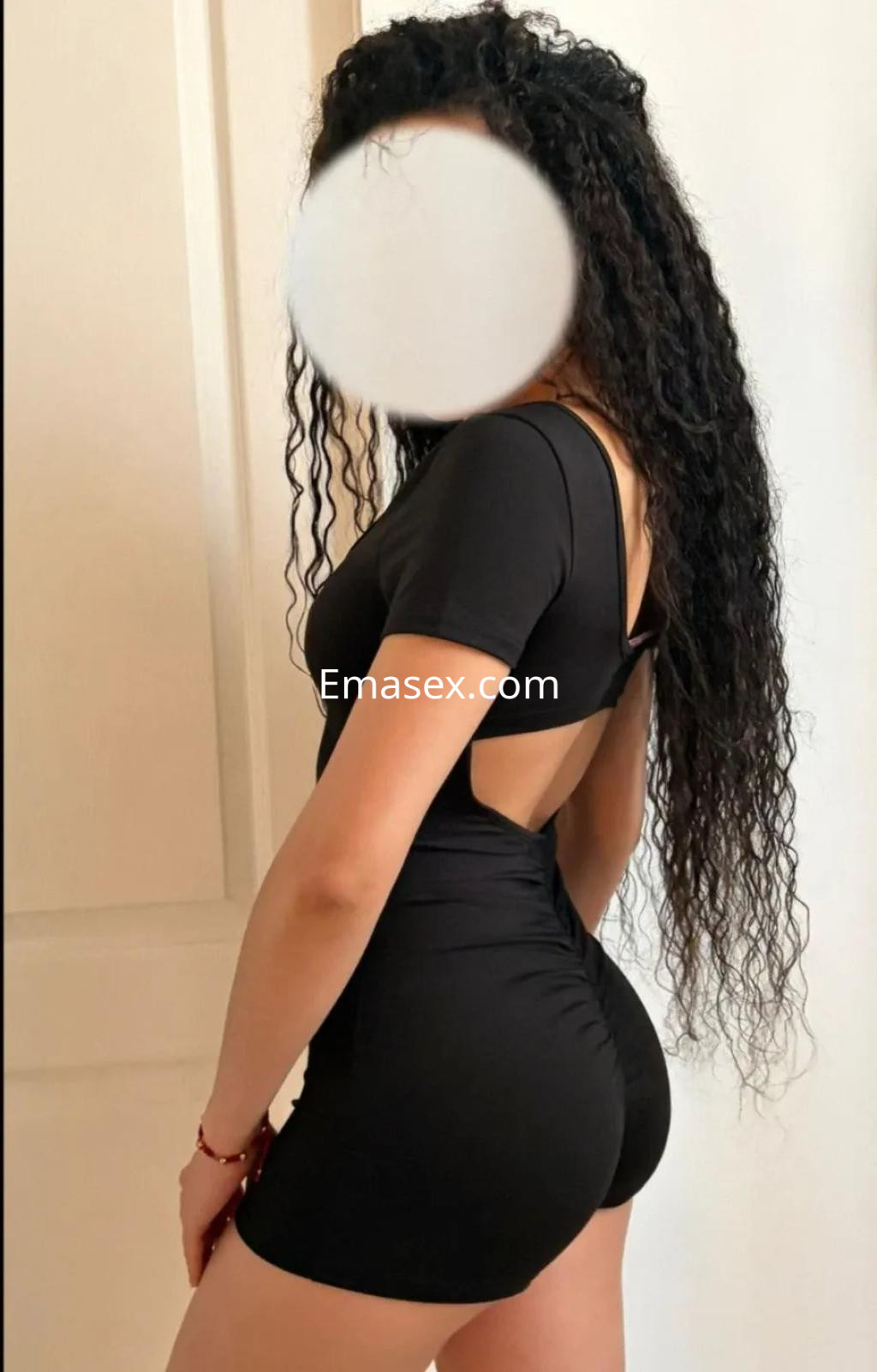 Escort en Madrid luciendo un vestido negro ajustado con escote en la espalda y cabello rizado.