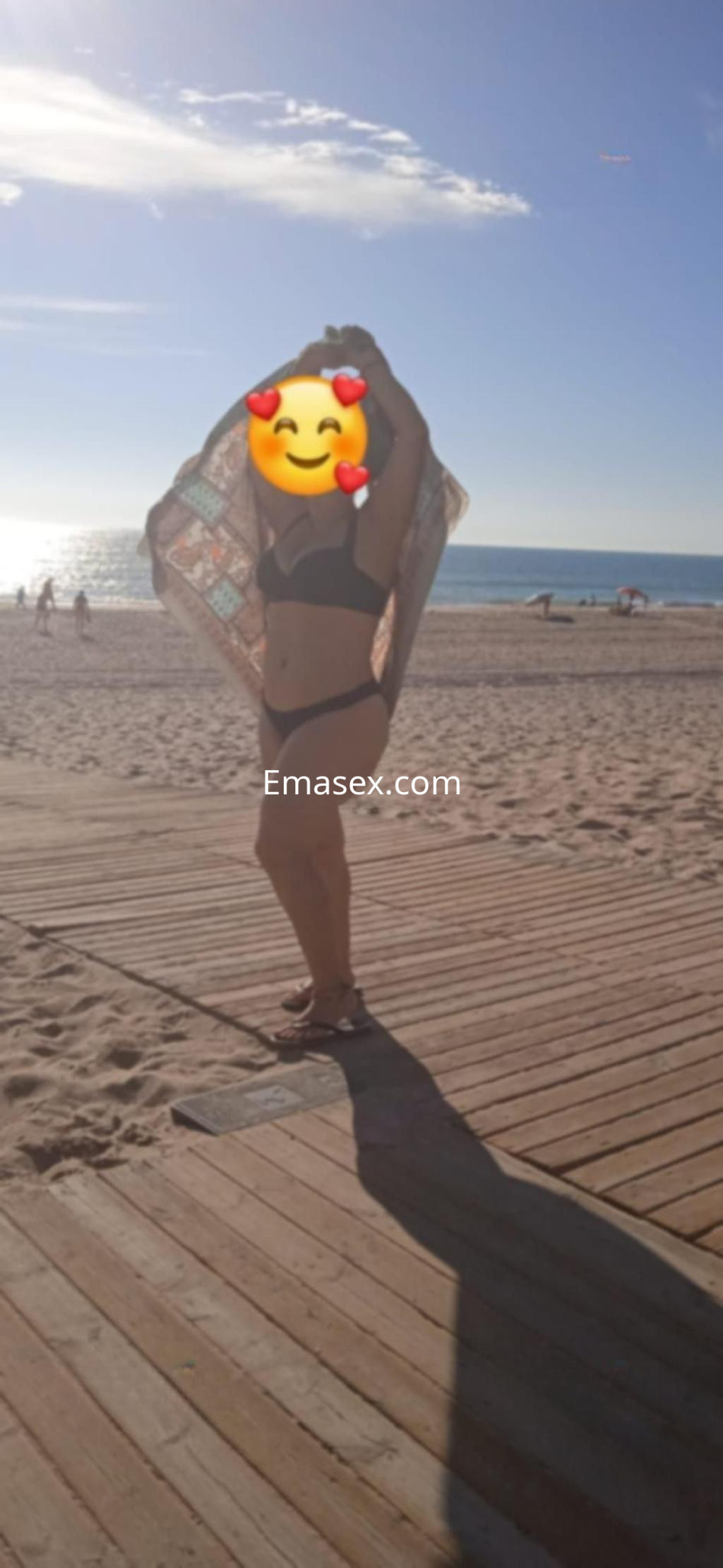 Escort en Madrid con cabello suelto, usando bikini y una toalla, posando en la playa bajo el sol.