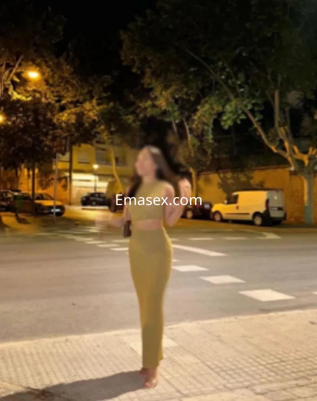 Escort de pie en la calle de Murcia, luciendo un vestido ajustado de color verde y con el cabello suelto.