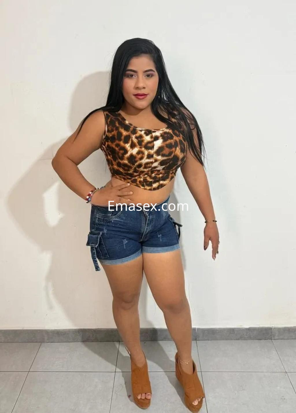Escort en Córdoba luciendo un top de leopardo con shorts de mezclilla y tacones, posando con confianza.