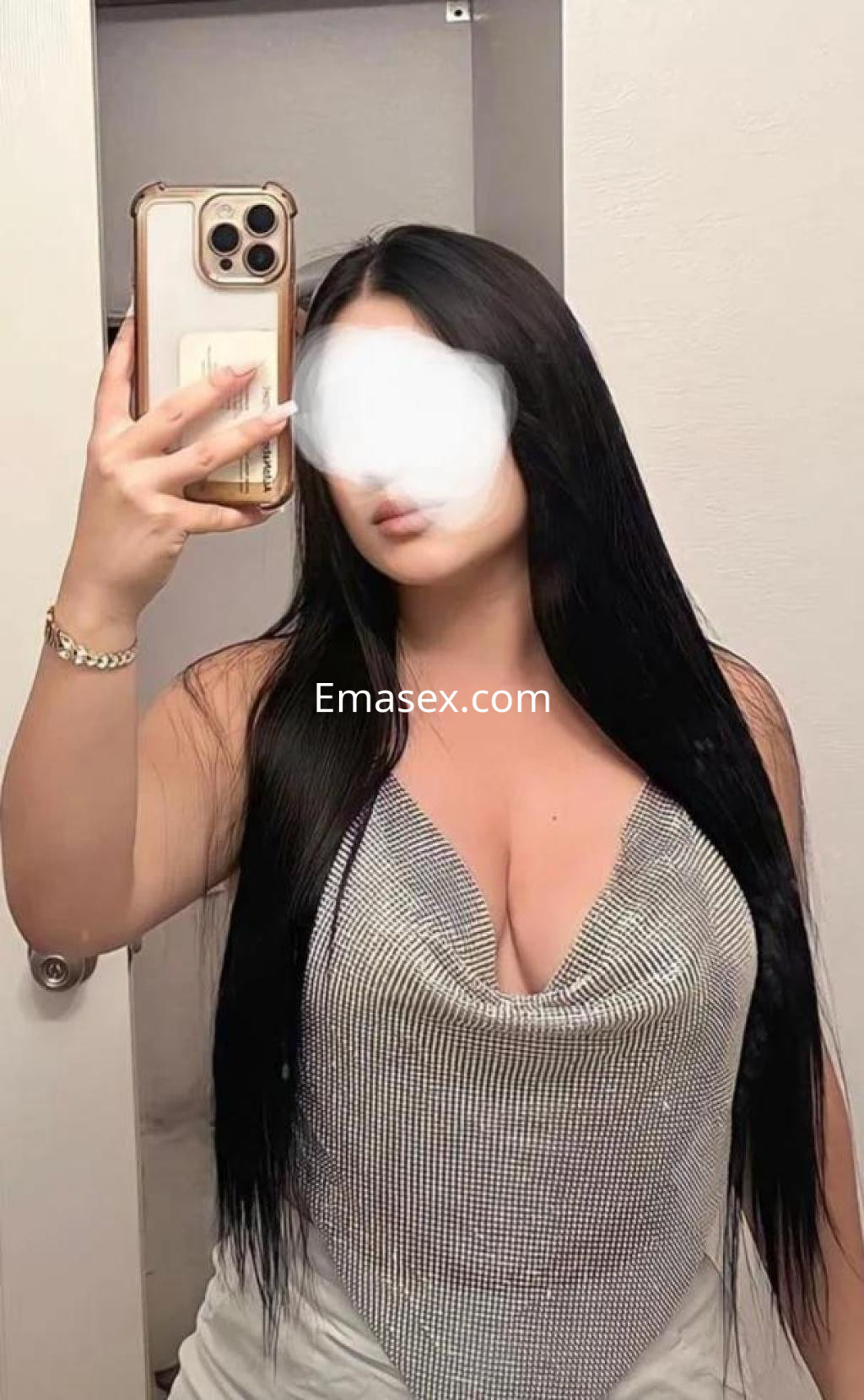 Escort en Murcia con cabello largo y oscuro, luciendo una blusa brillante y ajustada, posando frente a un espejo.