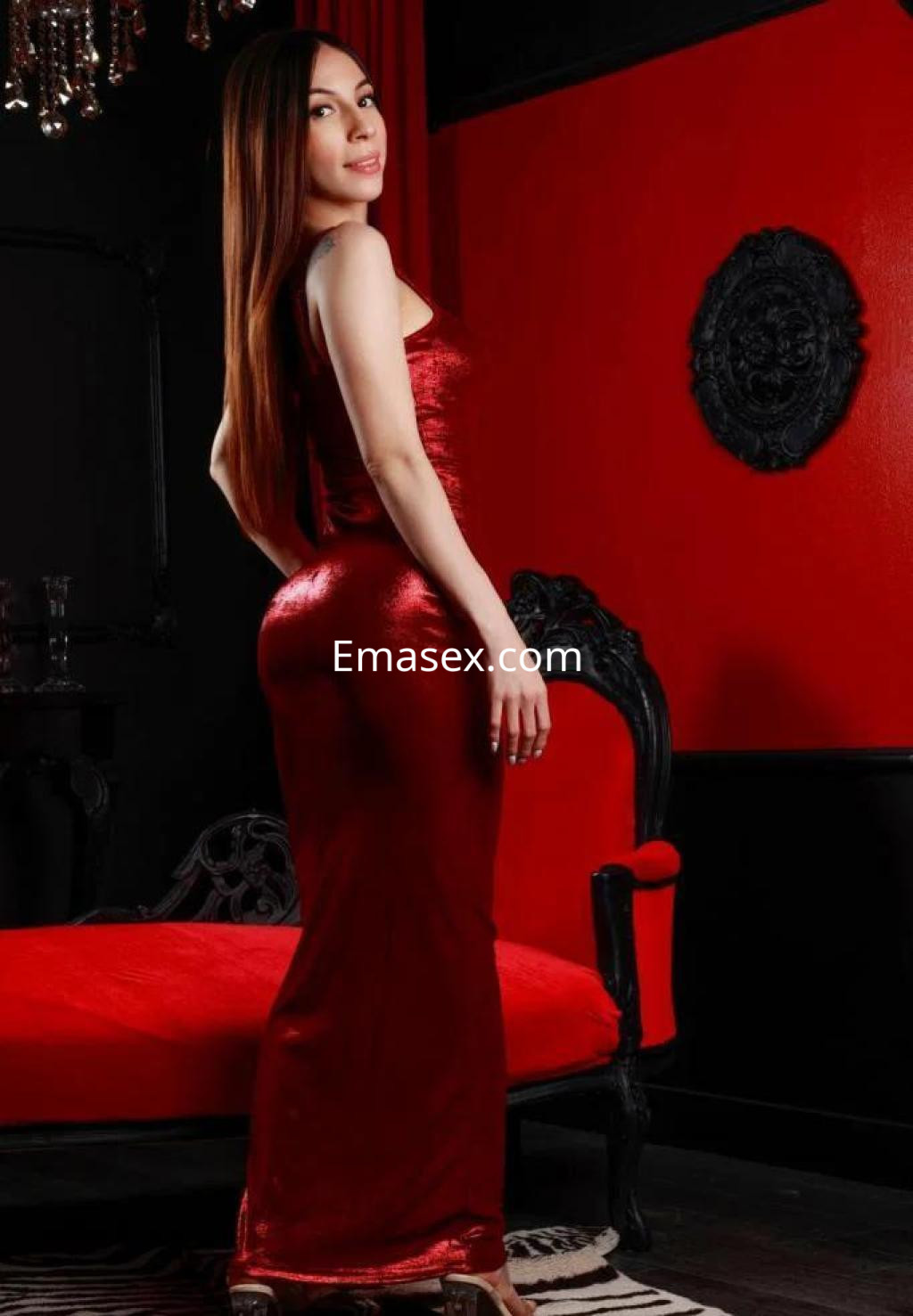 Puta en Zaragoza posando de perfil con un vestido rojo ajustado y cabello largo en un entorno elegante.
