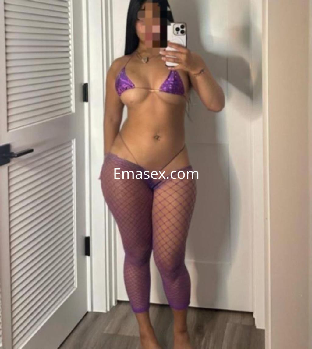 Escort en Toledo frente al espejo, luciendo un bikini brillante y mallas de red, con una pose confiada.