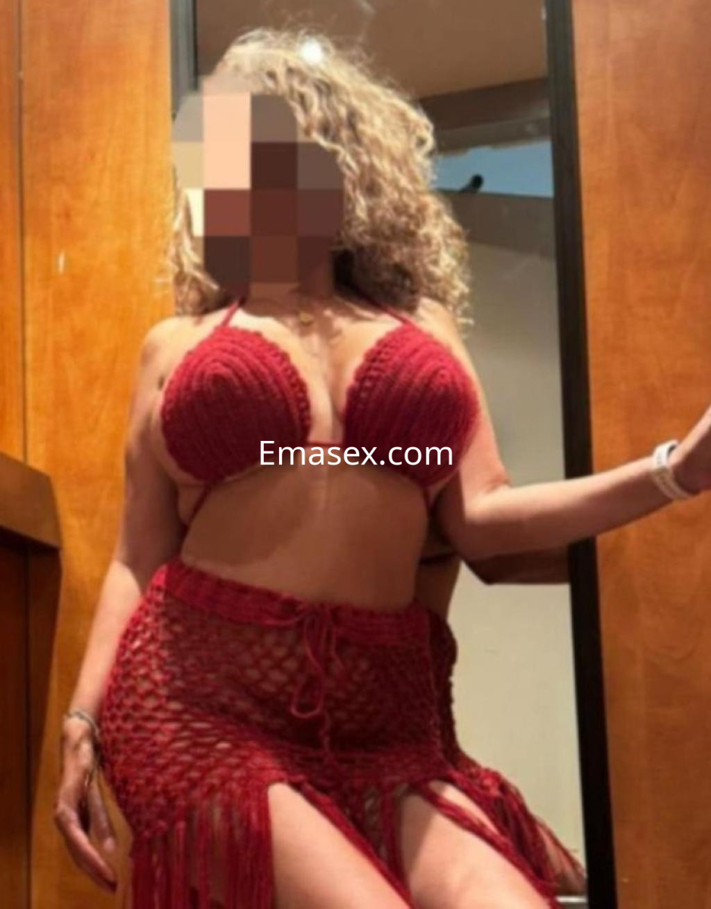 Puta en Alicante con cabello rizado, luciendo un conjunto de lencería rojo y una falda de red.