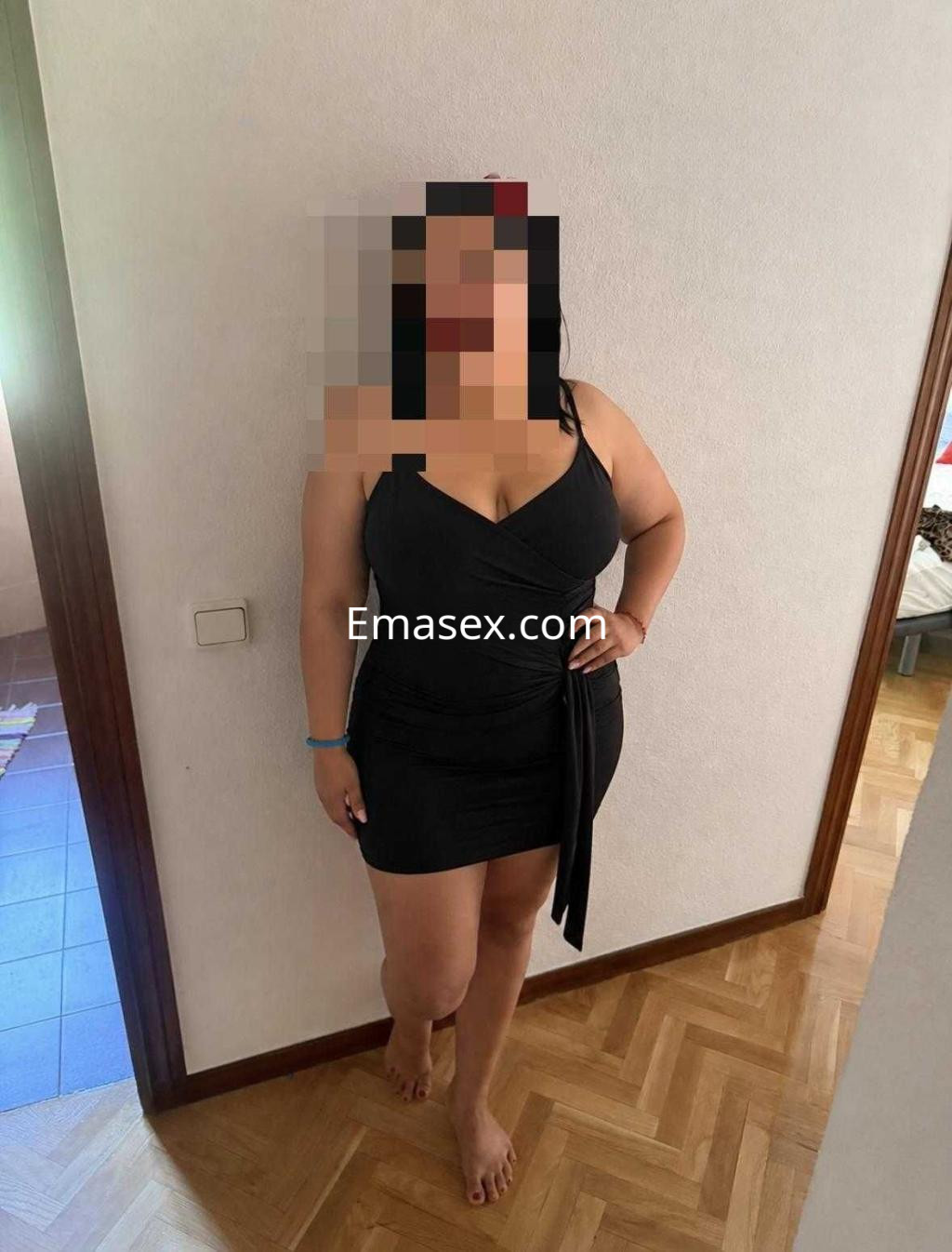 Escort en Toledo luciendo un vestido negro ajustado, con cabello oscuro y pose de pie en un ambiente interior.