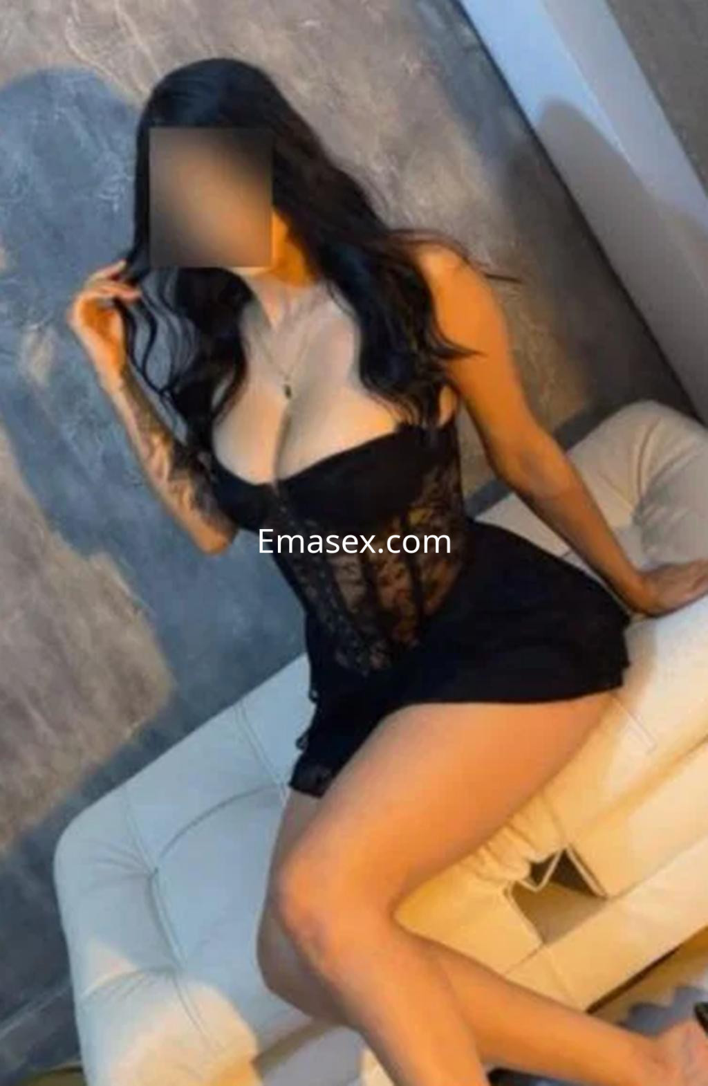 Escort en Logroño, posando en un sofá con lencería negra transparente y cabello largo y ondulado.