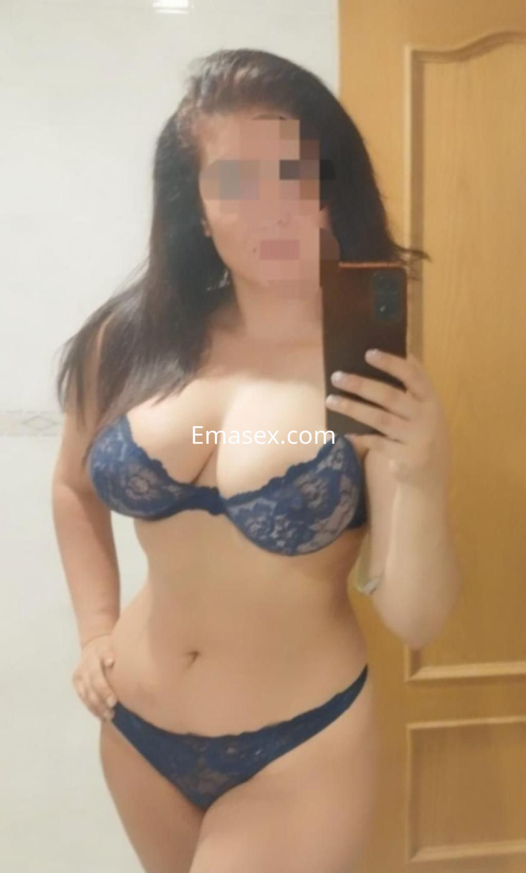 Escort en Madrid posando en lencería azul, con cabello oscuro y un fondo neutro de pared clara.